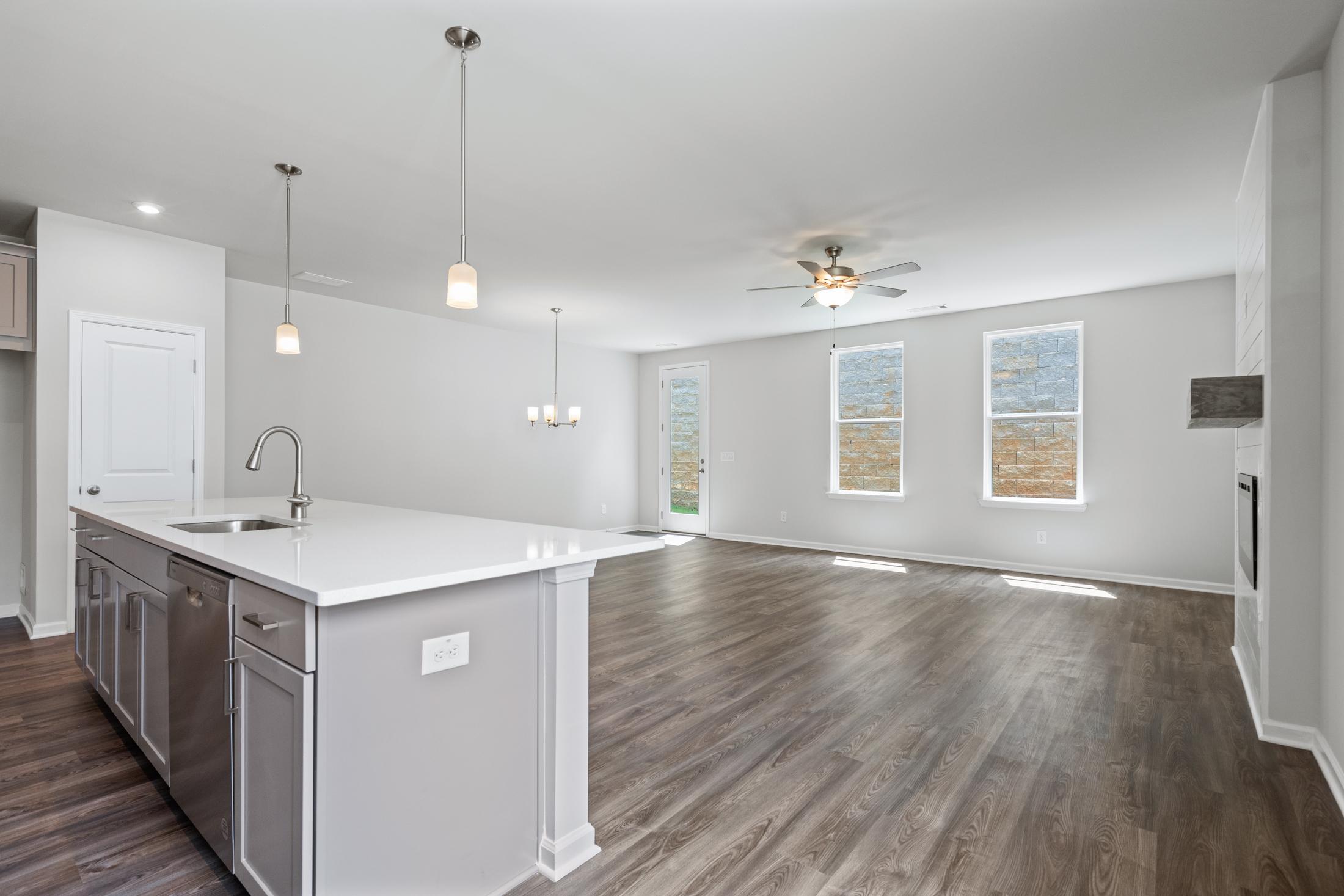 Open-concept kitchen in The Cary A home featuring white shaker cabinets, large quartz island with sink, hardwood floors, and large sunny windows