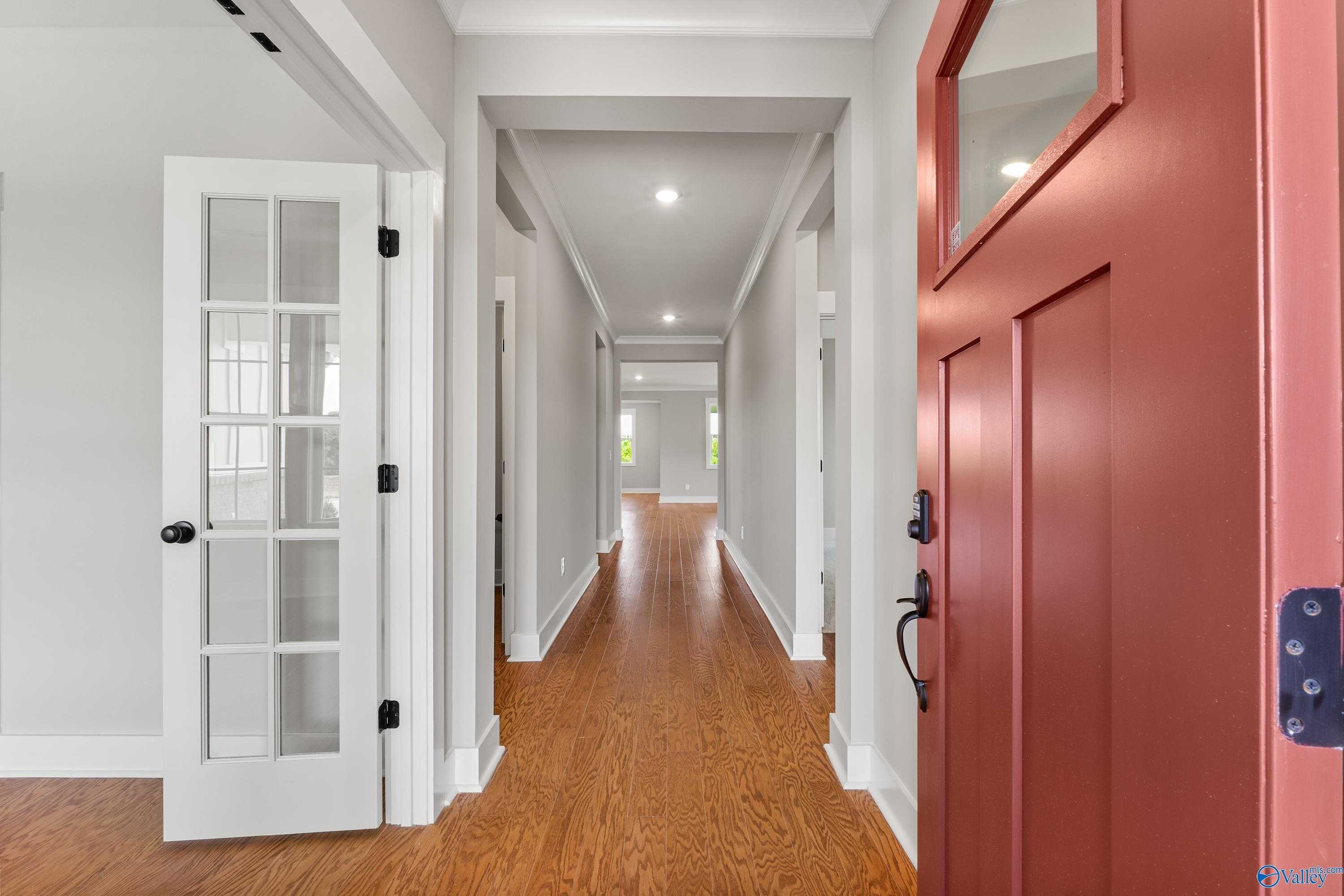 Spacious entry hallway with oak hardwood floors, glass French doors, and red front door in The Arcadia 4-bedroom home, Huntsville, Alabama