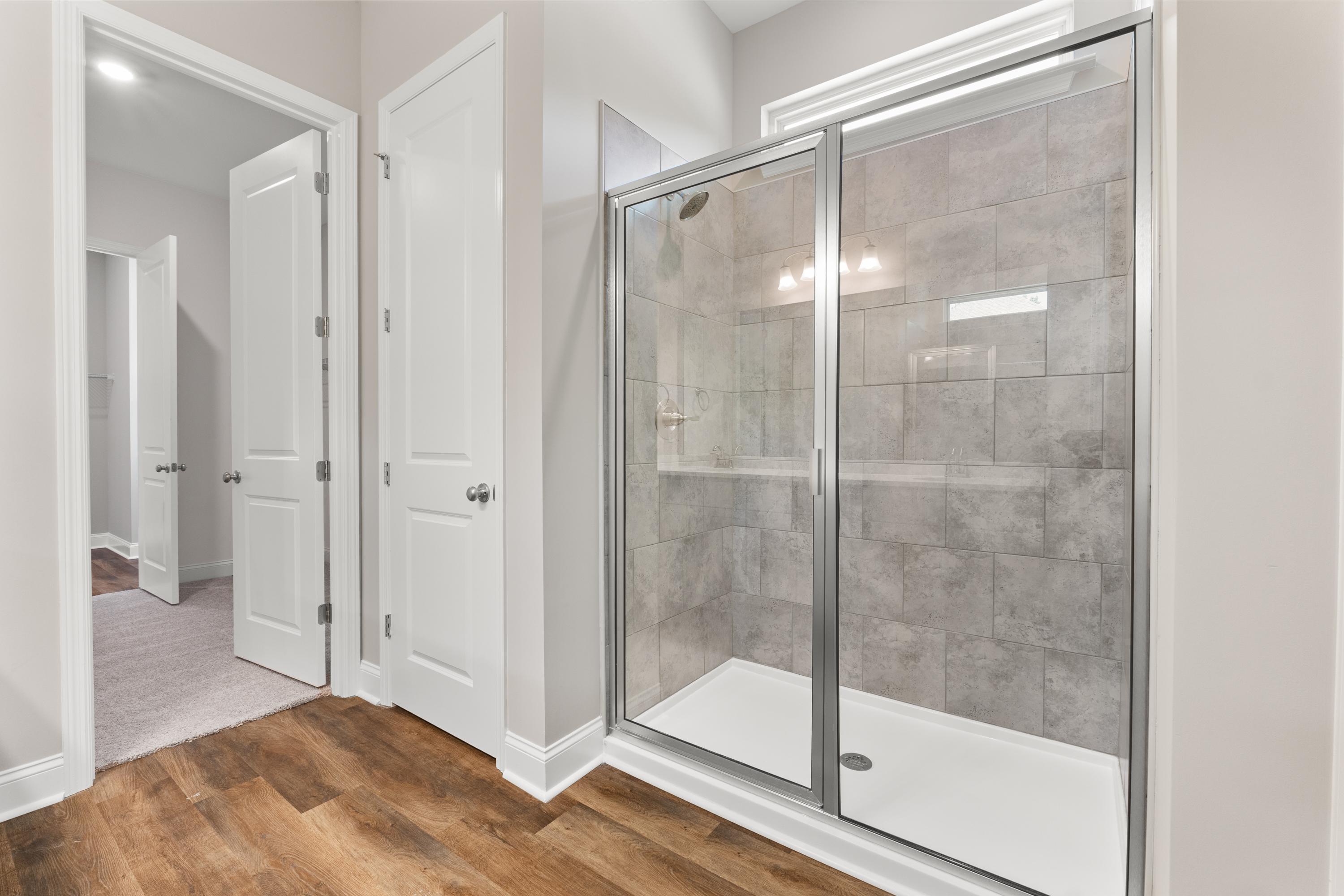 Spacious master bathroom in The Arcadia B with frameless glass shower, subway tile walls, and hardwood floors