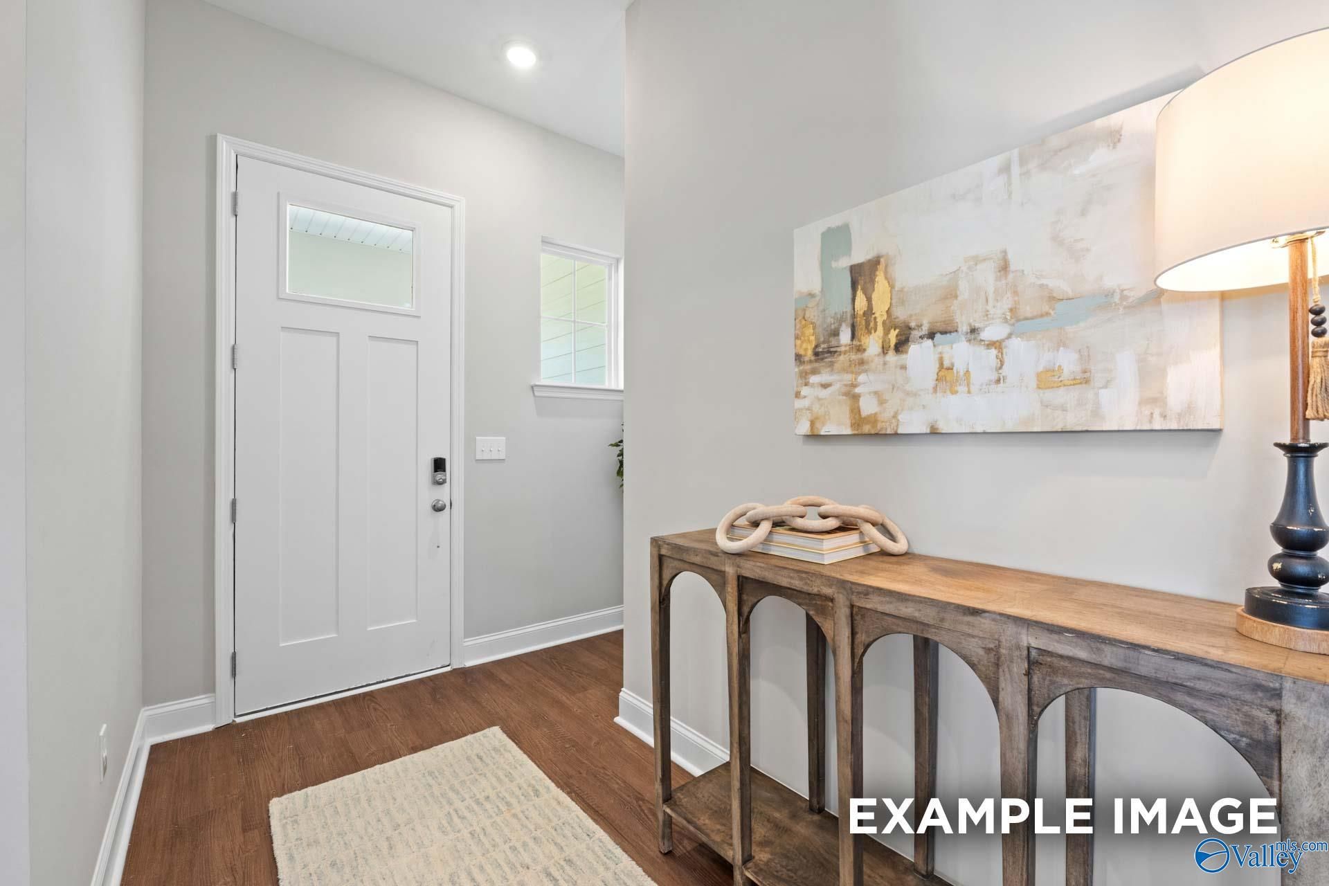 Elegant entry foyer with white glass-panel door, wooden arched console table, abstract art and lamp in Evermore Homes The Haven E, Owens Cross Roads, AL