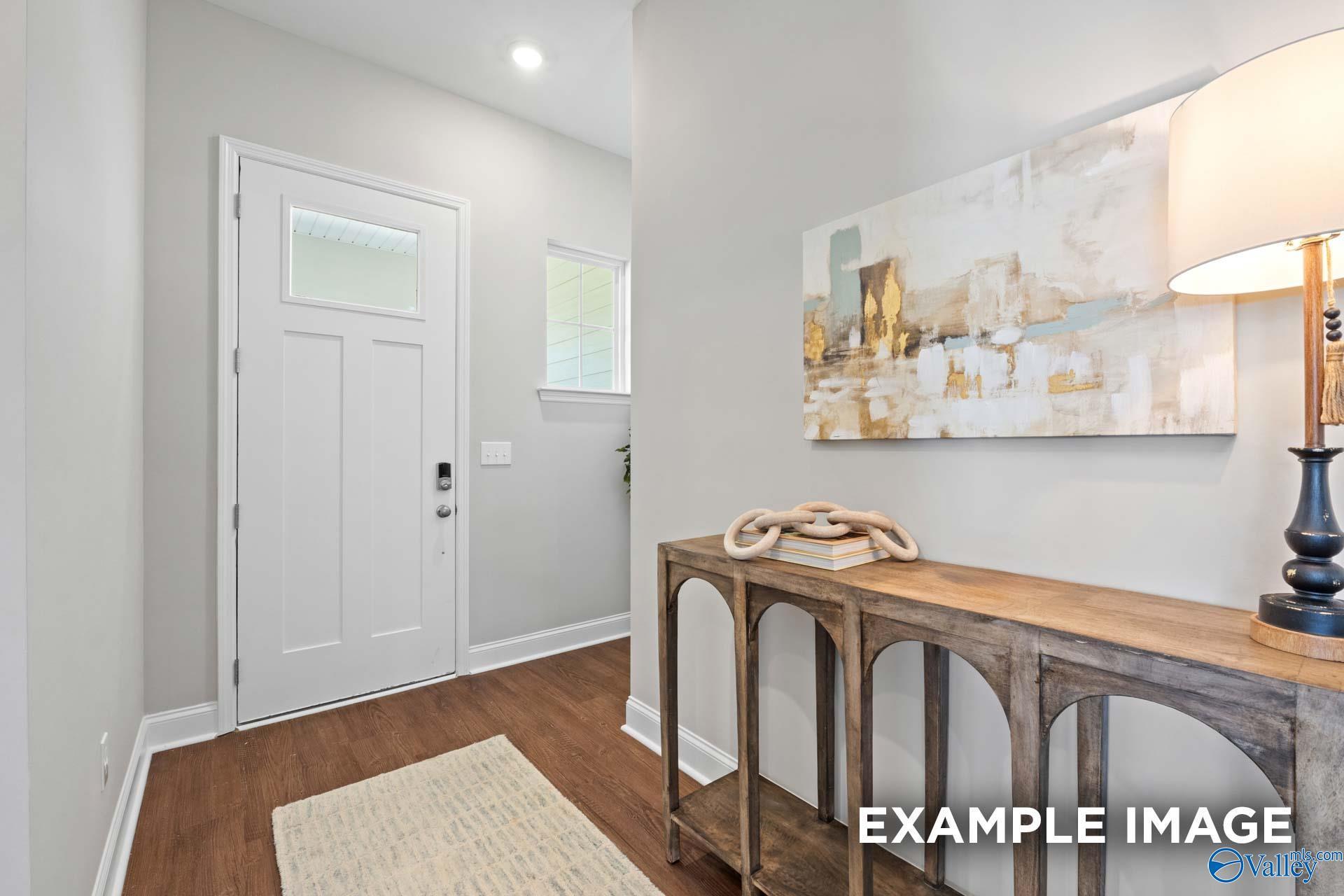Elegant entry foyer with white glass-panel door, wooden arched console table, abstract art and lamp in Evermore Homes The Haven E, Owens Cross Roads, AL