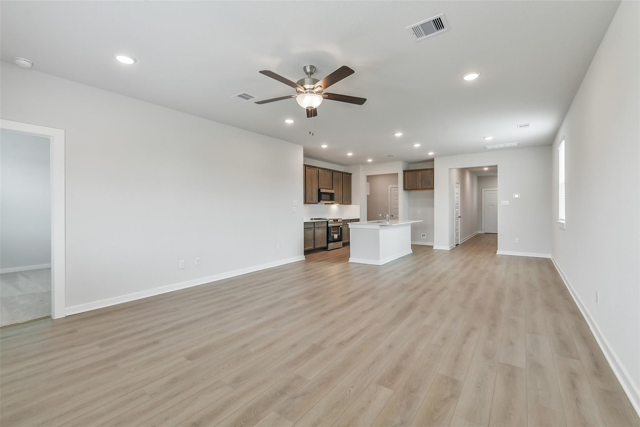Open-concept kitchen and living room with white island, cabinets, ceiling fans, and laminate floors in The Brazos E by Davidson Homes, Cleveland, TX
