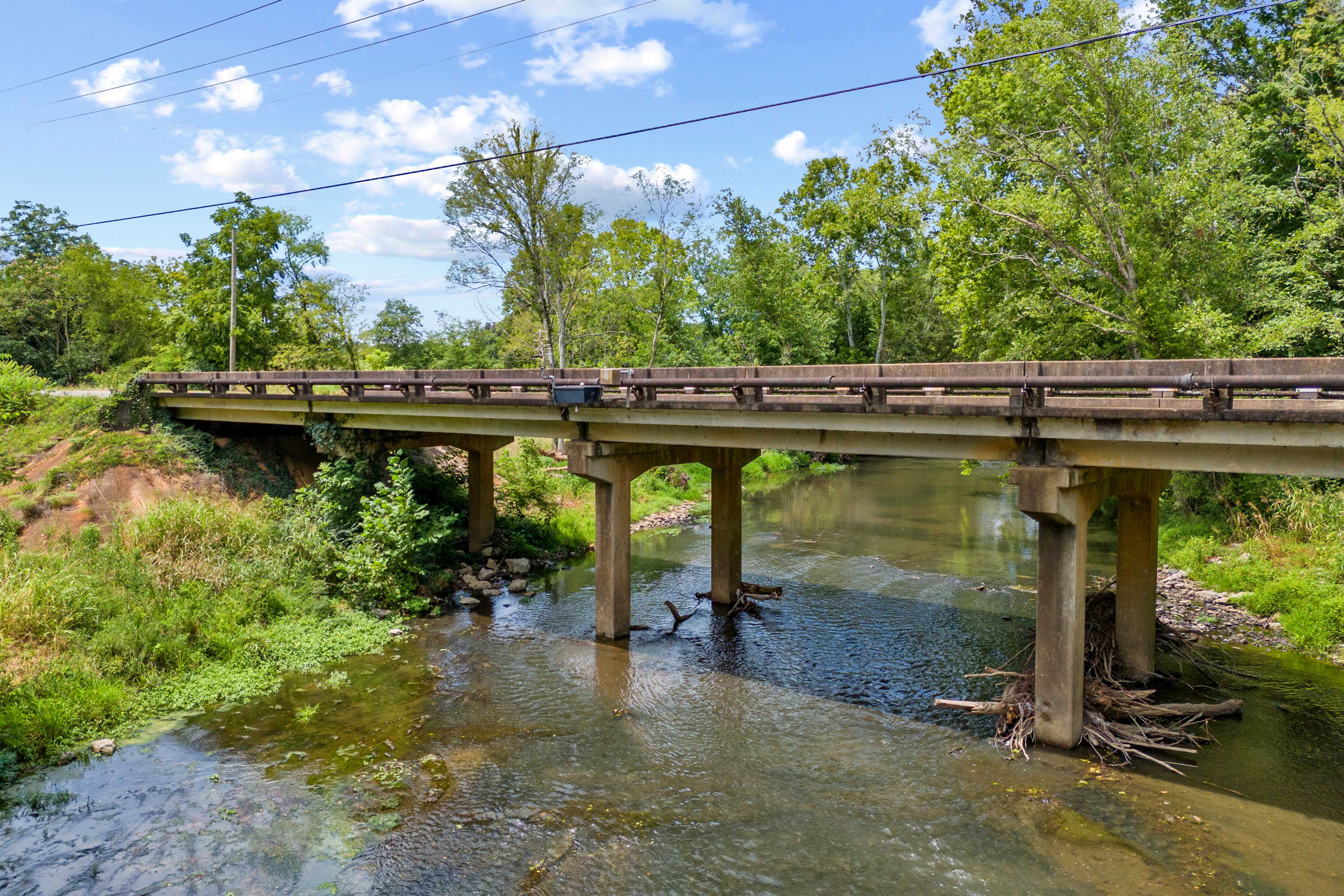 Rustic bridge over serene stream at The Meadows in Athens, Alabama, surrounded by lush green trees and foliage