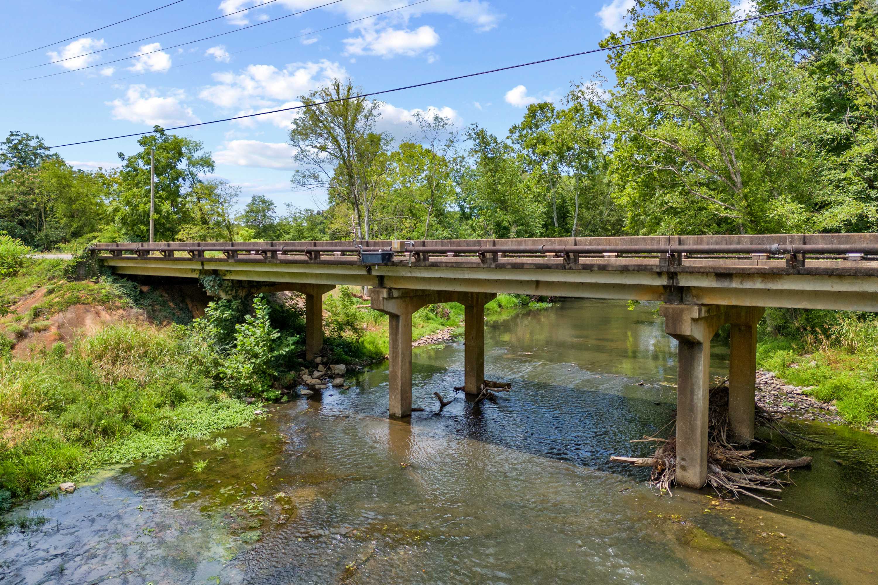 Rustic bridge over serene stream at The Meadows in Athens, Alabama, surrounded by lush green trees and foliage