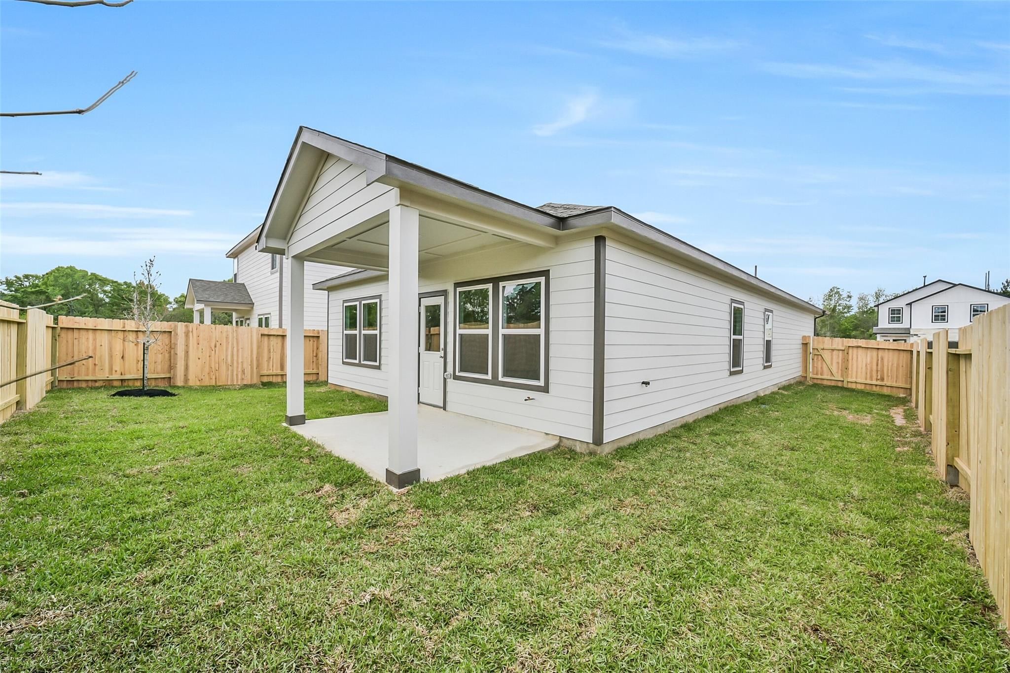 Covered back patio with white single-story home exterior, fenced green yard in Caney Creek Place, Conroe, Texas by Davidson Homes