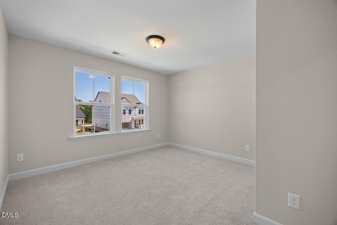 Bright empty bedroom with carpet and double windows overlooking neighborhood homes in Davidson Homes The Ashport M, Wendell Ridge, NC