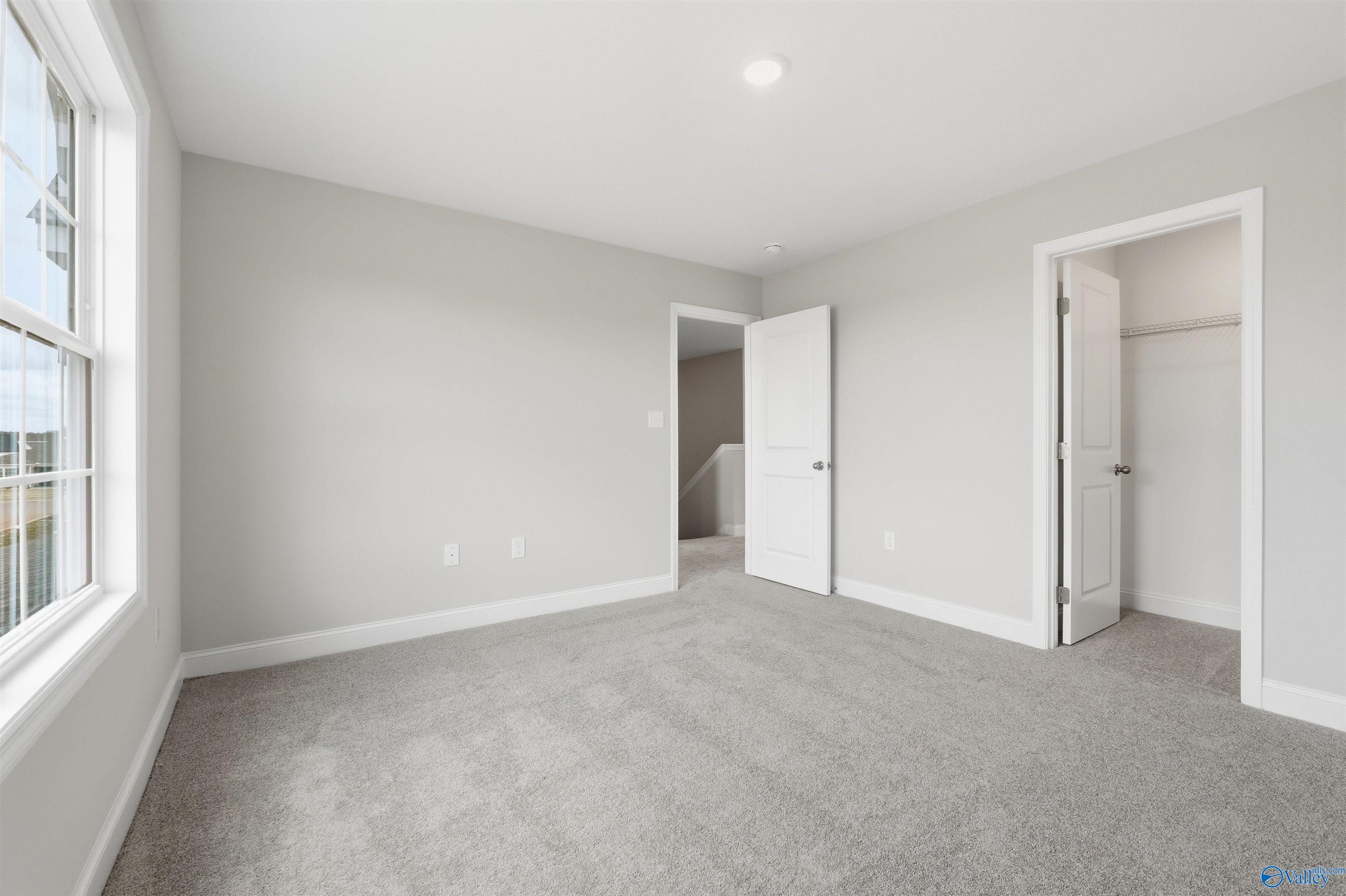 Bright, carpeted bedroom with walk-in closet in The Shelby D floor plan at Evergreen Mill, Madison, Alabama.