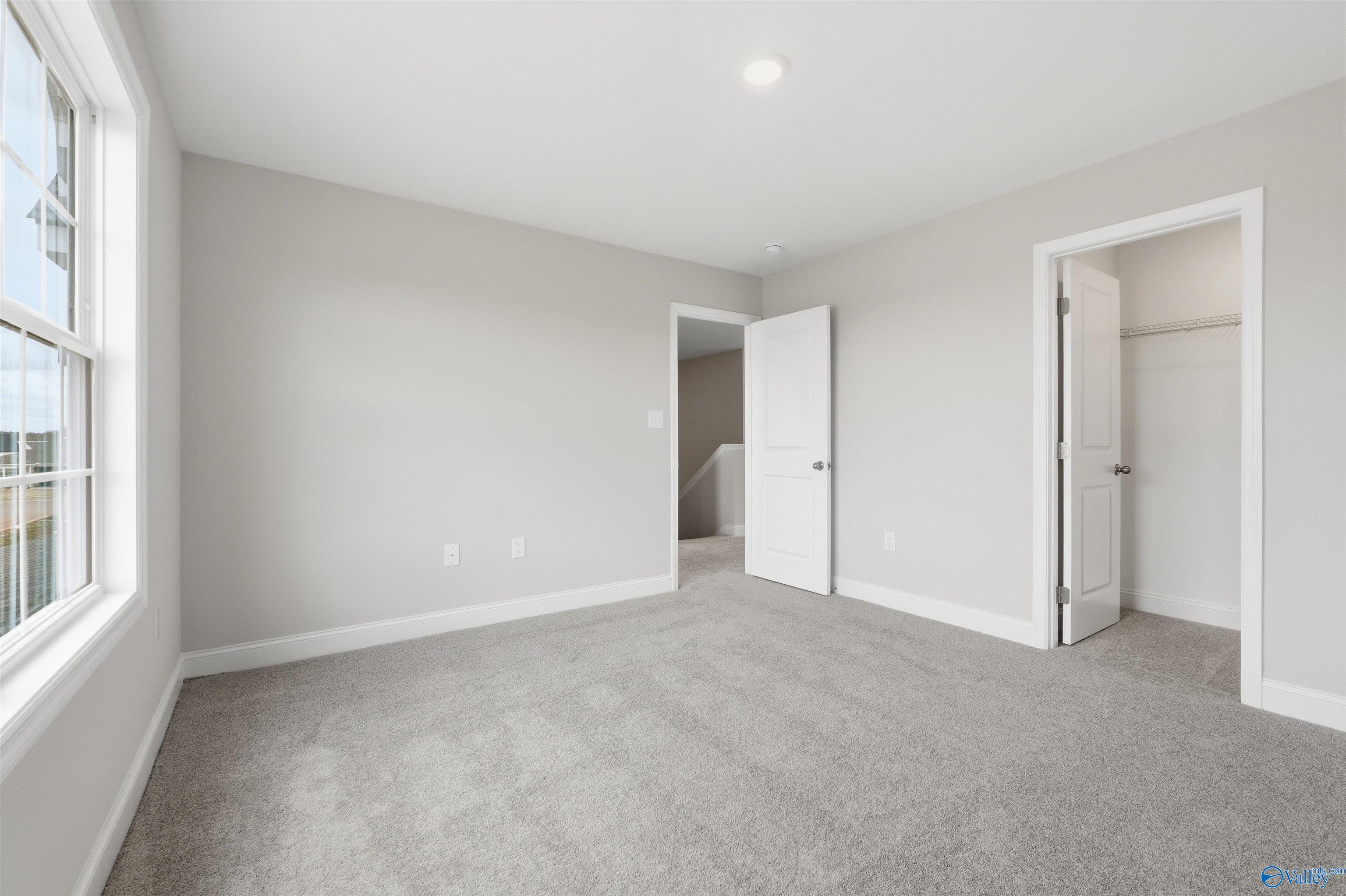 Bright, carpeted bedroom with walk-in closet in The Shelby D floor plan at Evergreen Mill, Madison, Alabama.