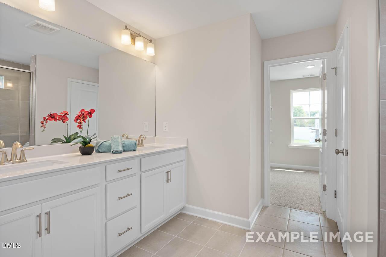 Luxurious master bathroom double vanity with white cabinets, gold faucets, orchids, and shower in The Willow D, Lillington NC