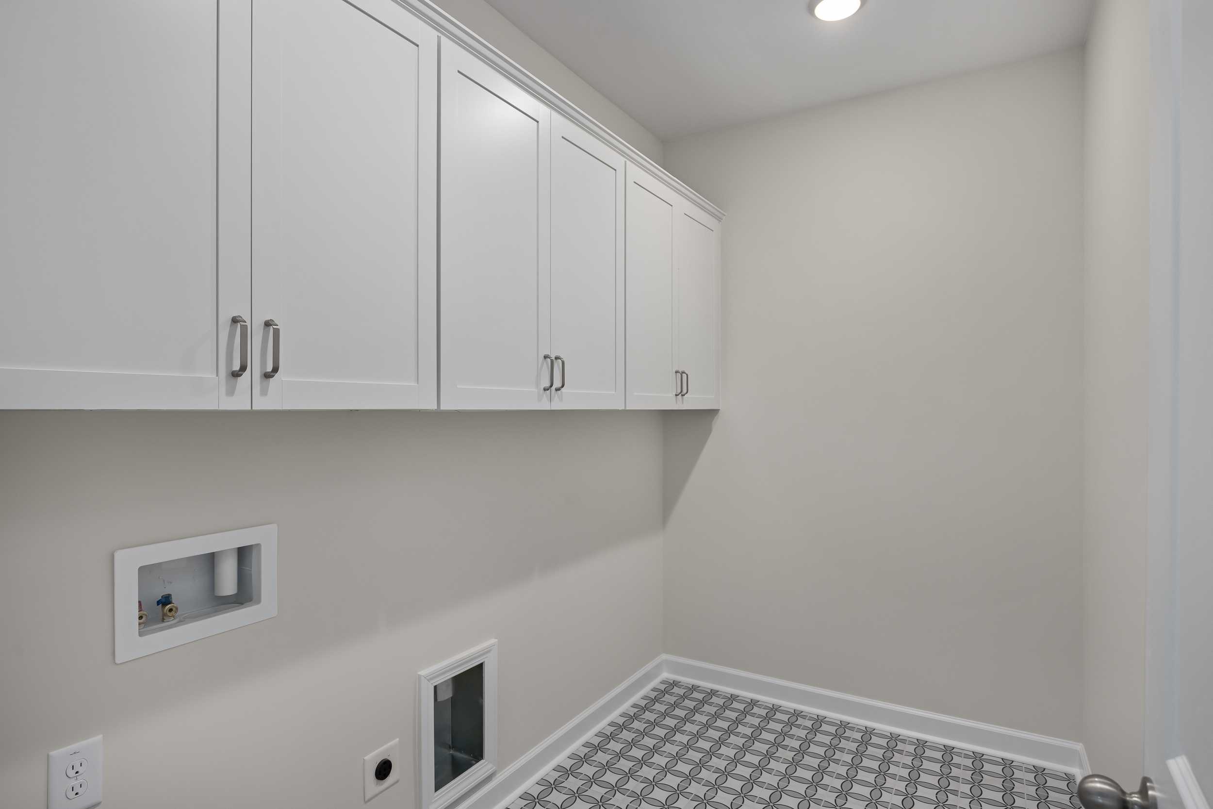 Spacious laundry room in The Beech C featuring white shaker cabinets, washer dryer hookups, and gray tiled flooring