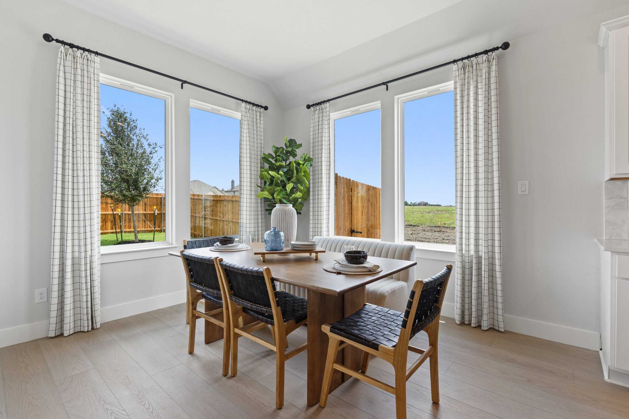 Bright dining room with wooden table, rattan chairs, and large windows overlooking fenced backyard in Davidson Homes Sequoia N, Josephine, TX