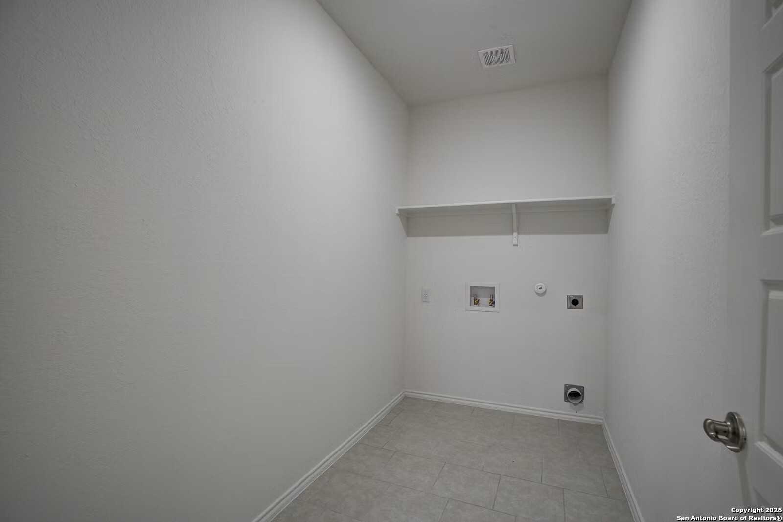 Spacious white laundry room with tiled floor, built-in shelves, and washer-dryer hookups in The Douglas B, Hannah Heights, Seguin, Texas