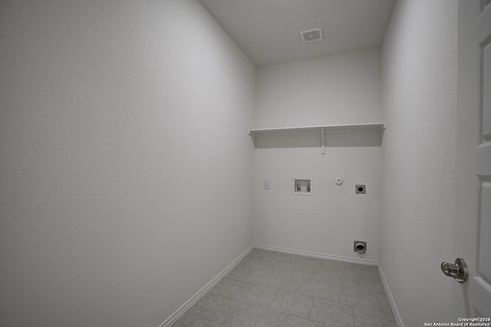 Spacious white laundry room with tiled floor, built-in shelves, and washer-dryer hookups in The Douglas B, Hannah Heights, Seguin, Texas
