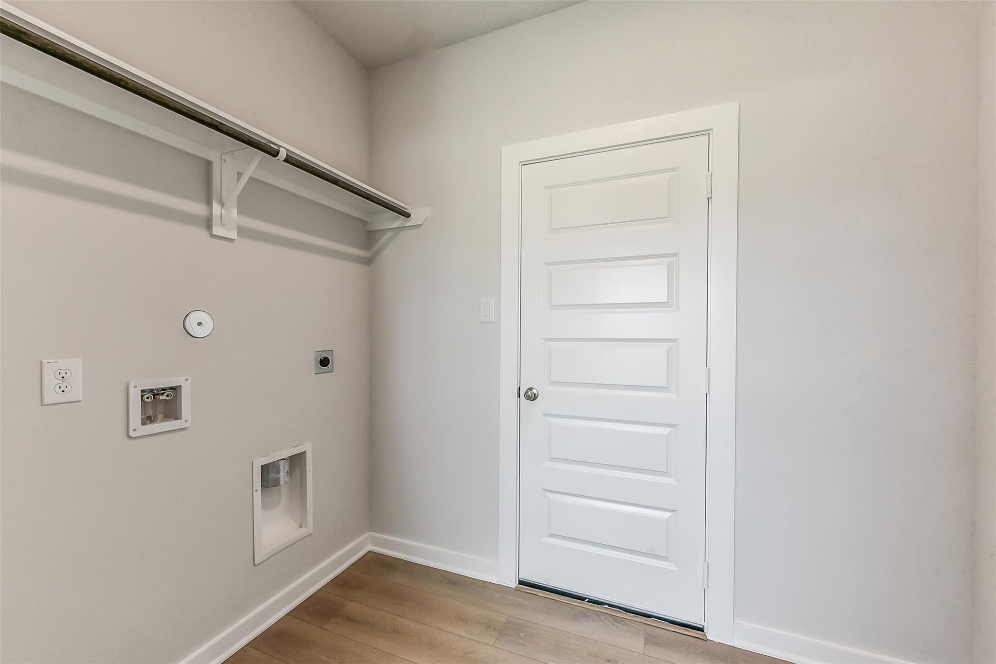 Modern laundry room with hanging rod, washer/dryer hookups, white paneled door in Davidson Homes The Sabine F, Dayton Texas