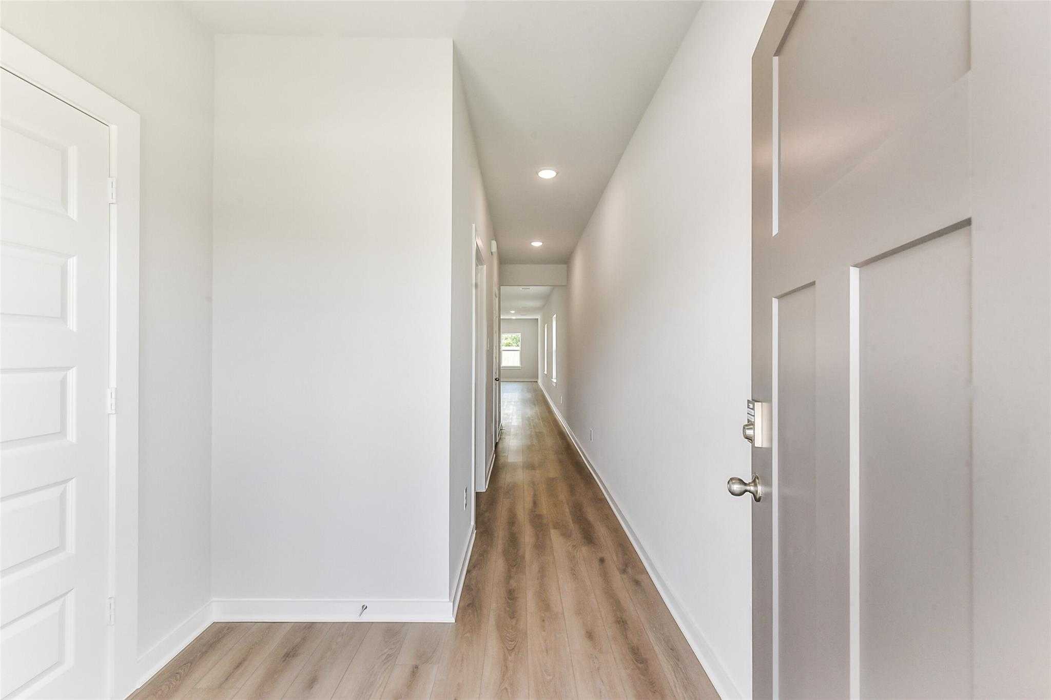 Bright hallway with light wood floors and white walls in Davidson Homes The Frio F, Dayton, Texas