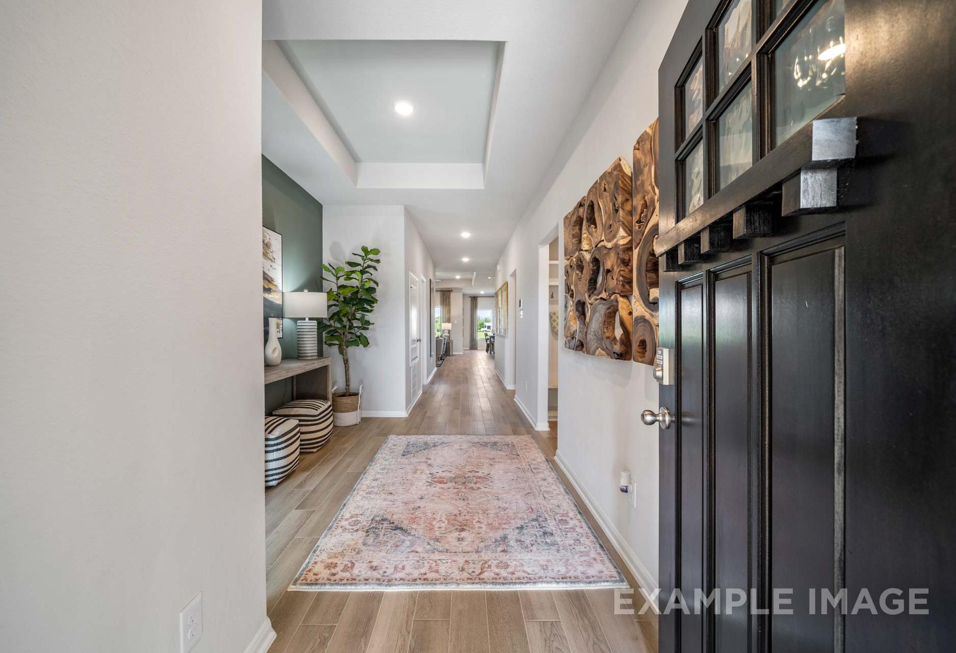 Spacious hallway in The Acadia A home design with hardwood floors, neutral walls, wooden art, and black front door