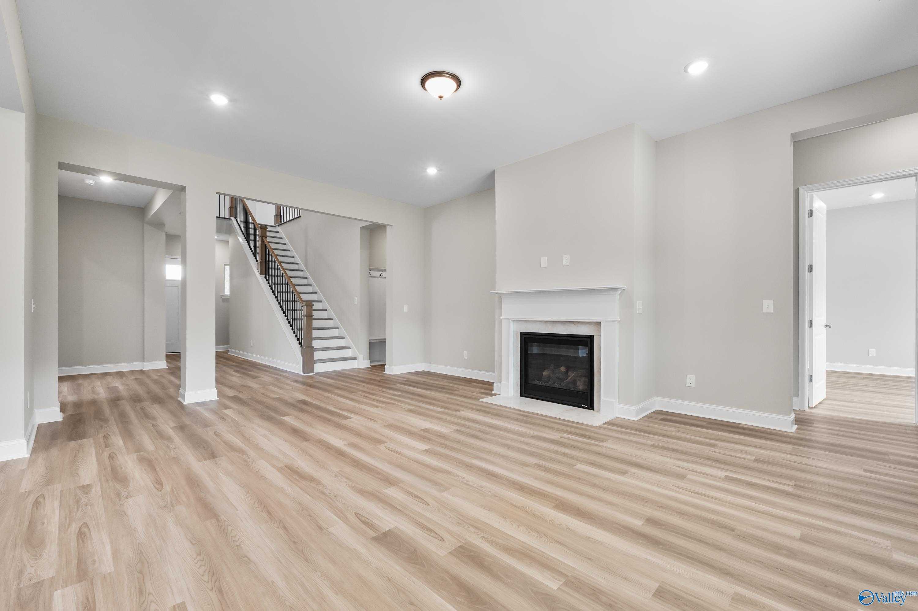 Open living room with modern gas fireplace, hardwood floors, and staircase in The Haven 5-bedroom home, Owens Cross Roads, Alabama