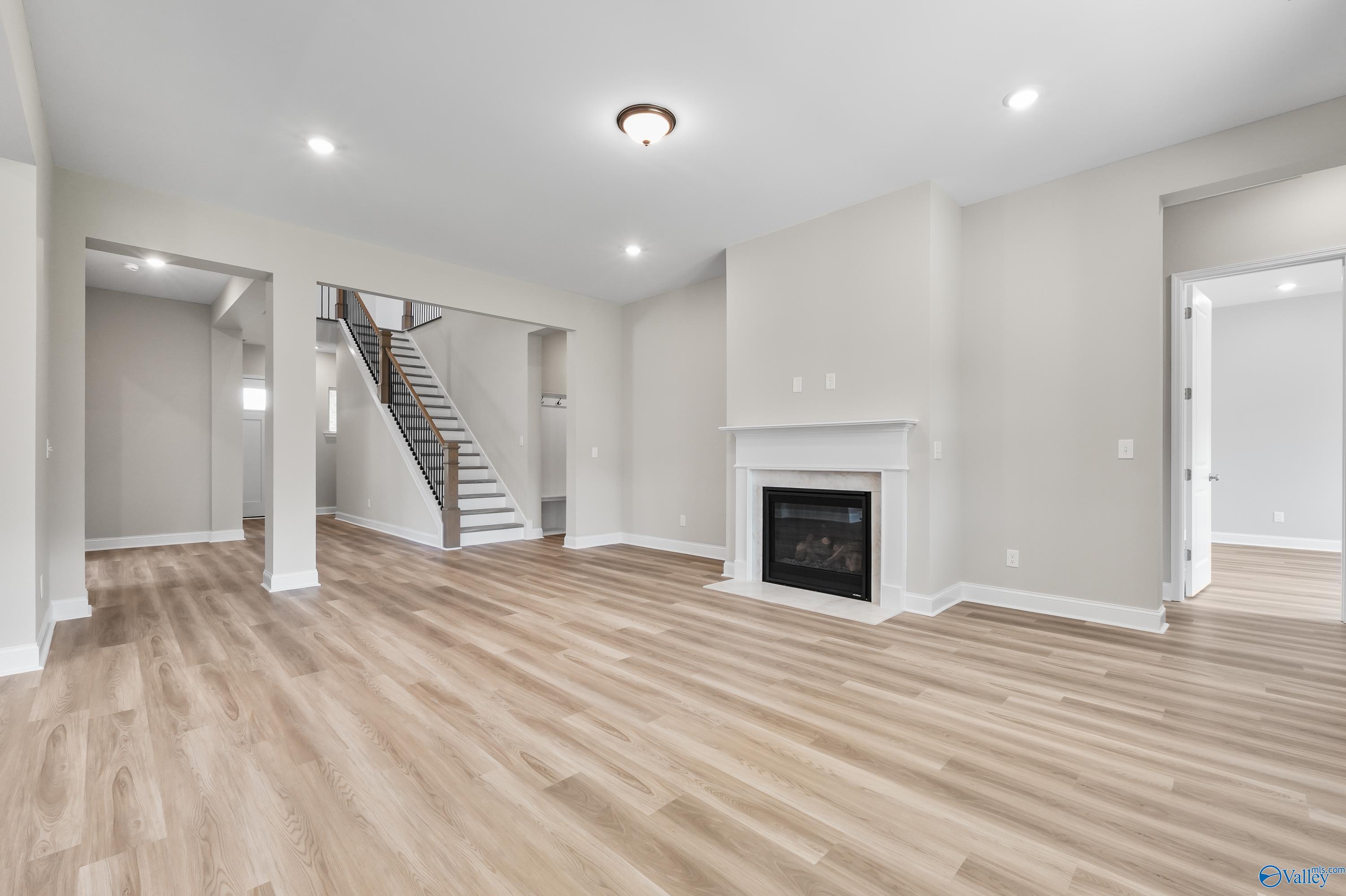 Open living room with modern gas fireplace, hardwood floors, and staircase in The Haven 5-bedroom home, Owens Cross Roads, Alabama