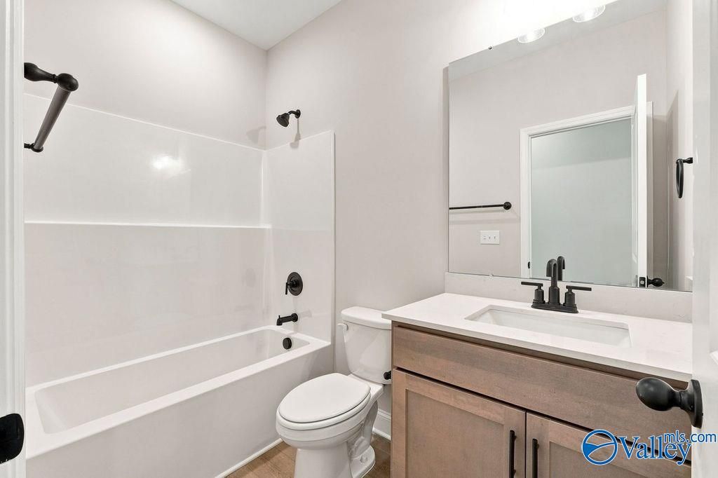 Modern white bathroom with tub, toilet, and wood vanity with black fixtures in Davidson Homes' Rockford floor plan, Hartselle, Alabama