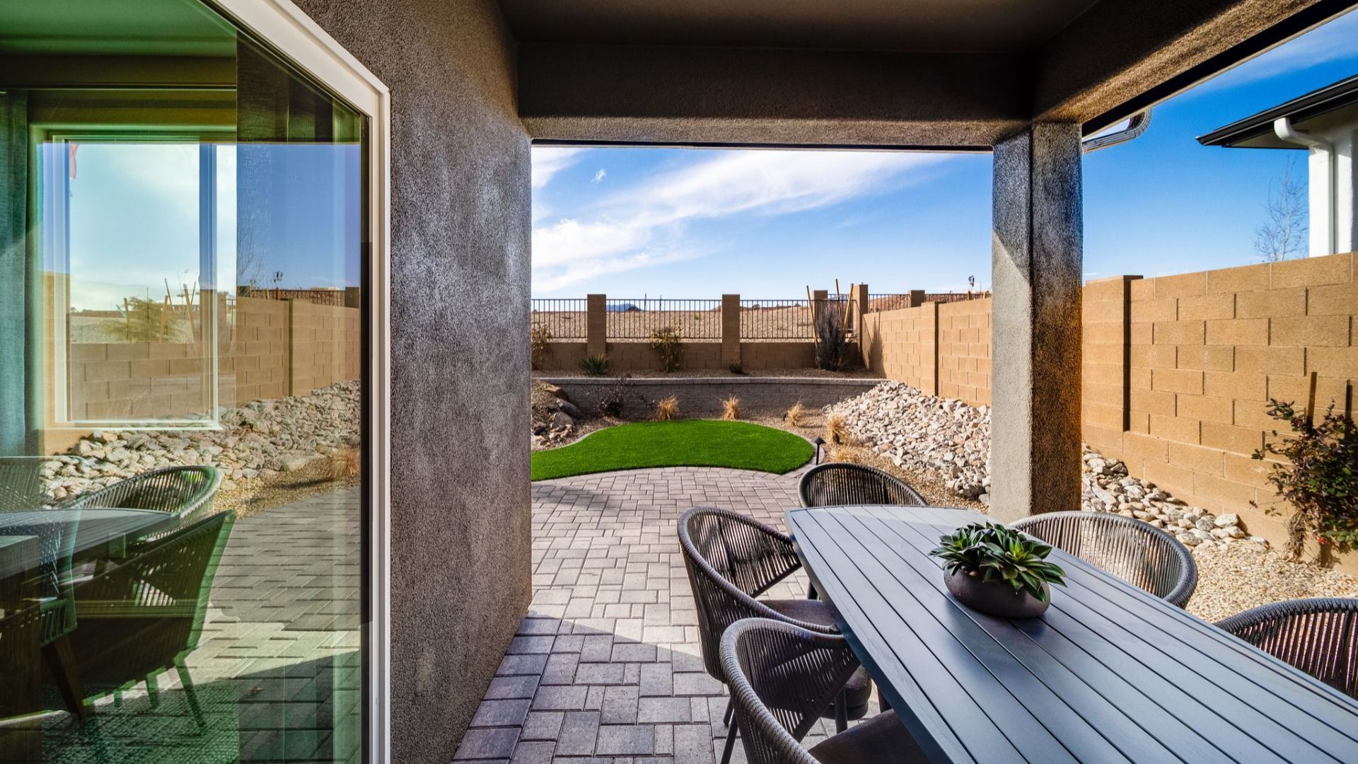 Covered patio at Vineyards at Cottonwood in Cottonwood AZ with wicker dining set, paver floor, turf lawn, and desert rock landscaping