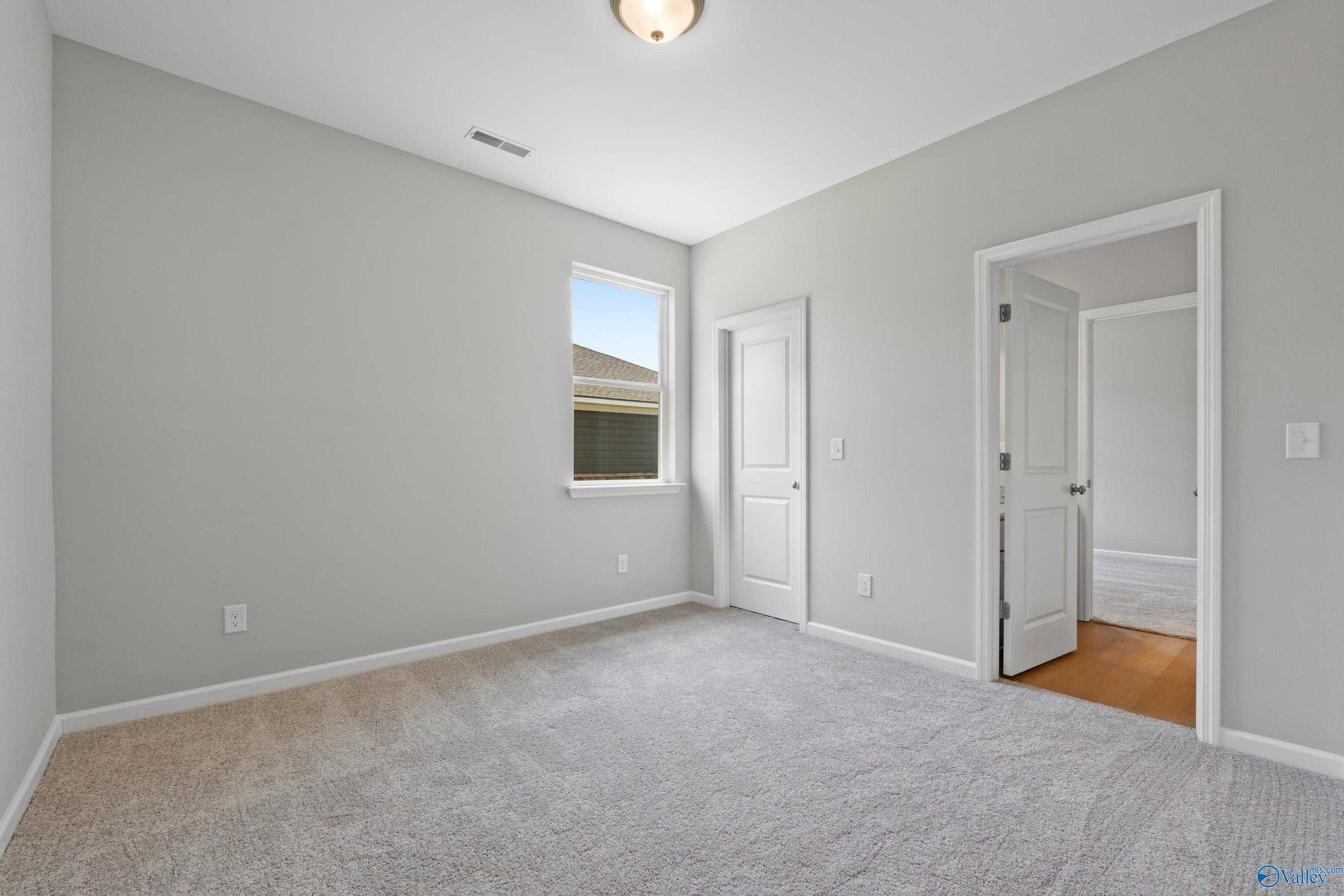 Spacious secondary bedroom with gray walls, plush carpet, window blinds, and adjacent bath door in Davidson Homes The Orion, Athens Alabama