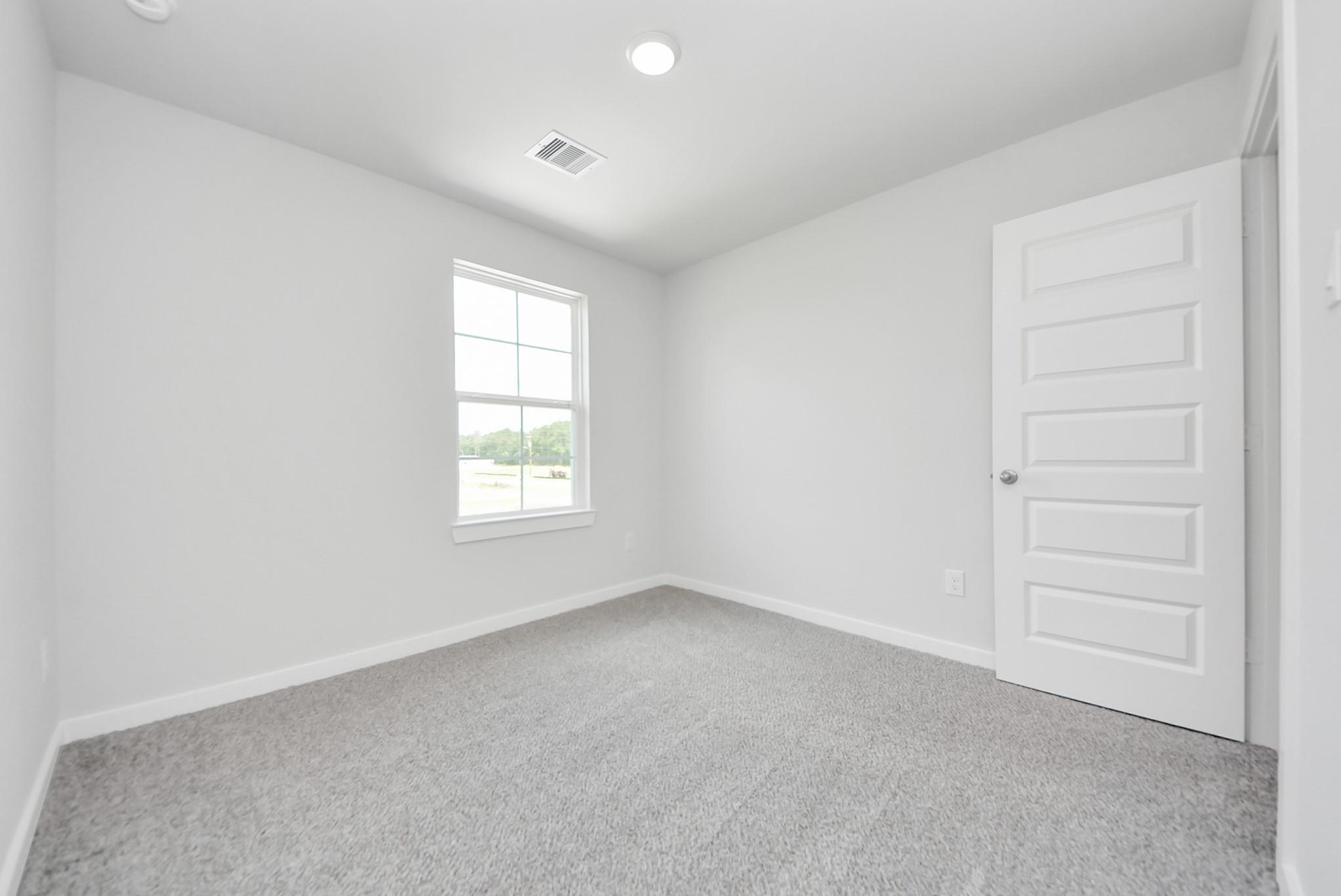 Bright, carpeted bedroom with neutral walls and a white door in The Blanco F floor plan at Spring Branch Crossing, Conroe.