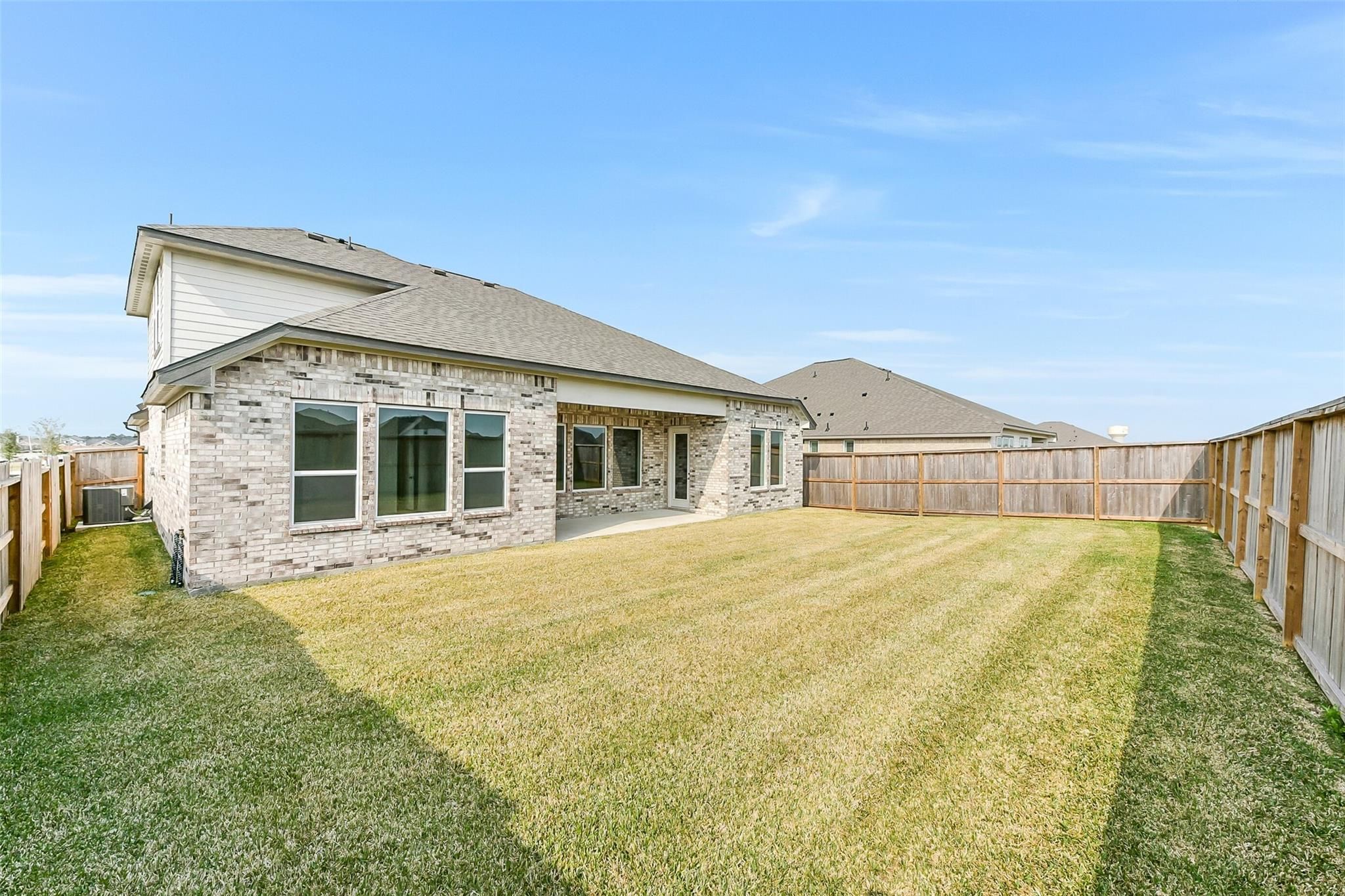 Expansive grassy backyard with wooden fence behind brick 3-bedroom Edward A home by Davidson Homes in Lago Mar, Texas City