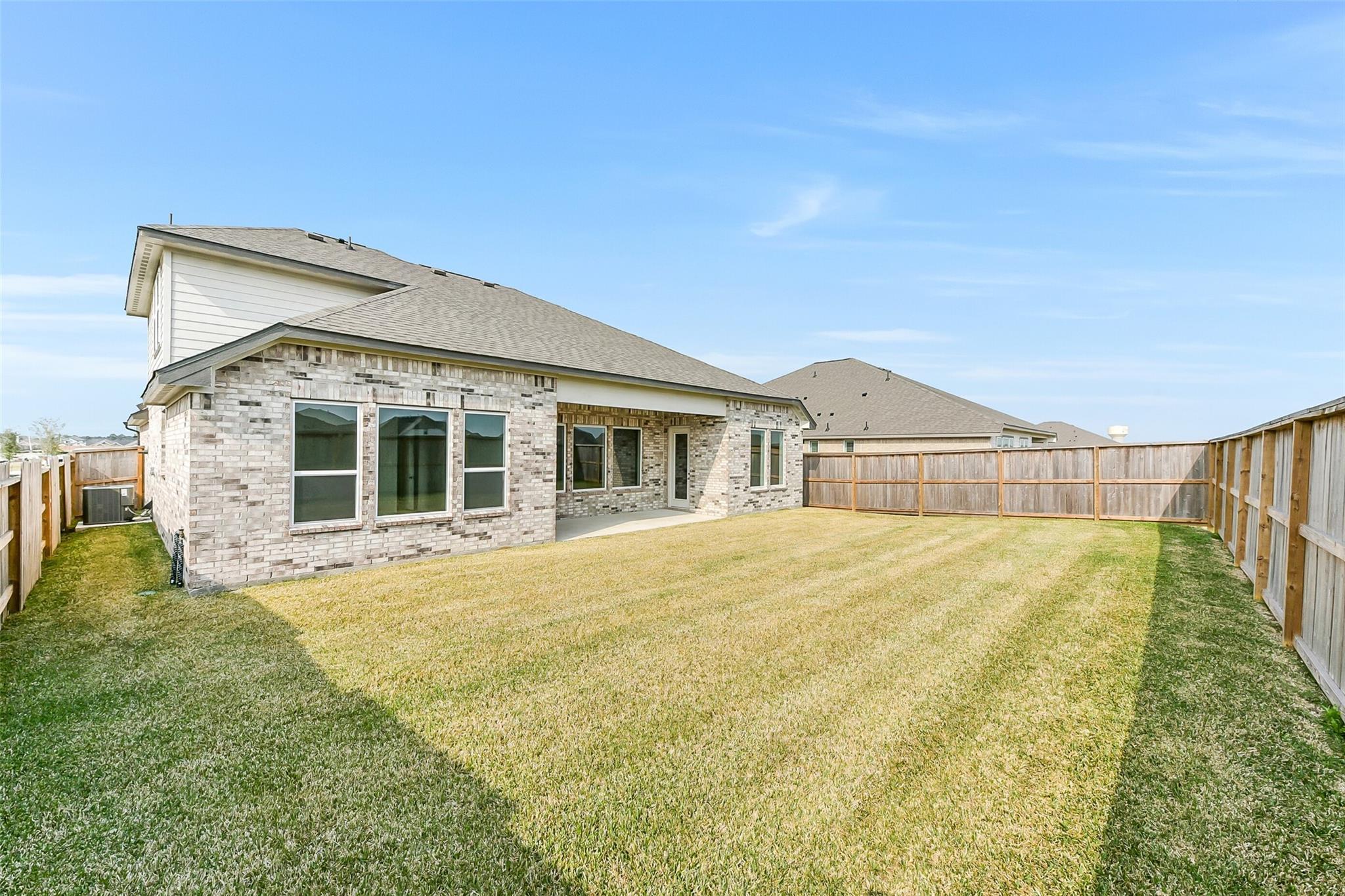 Expansive grassy backyard with wooden fence behind brick 3-bedroom Edward A home by Davidson Homes in Lago Mar, Texas City