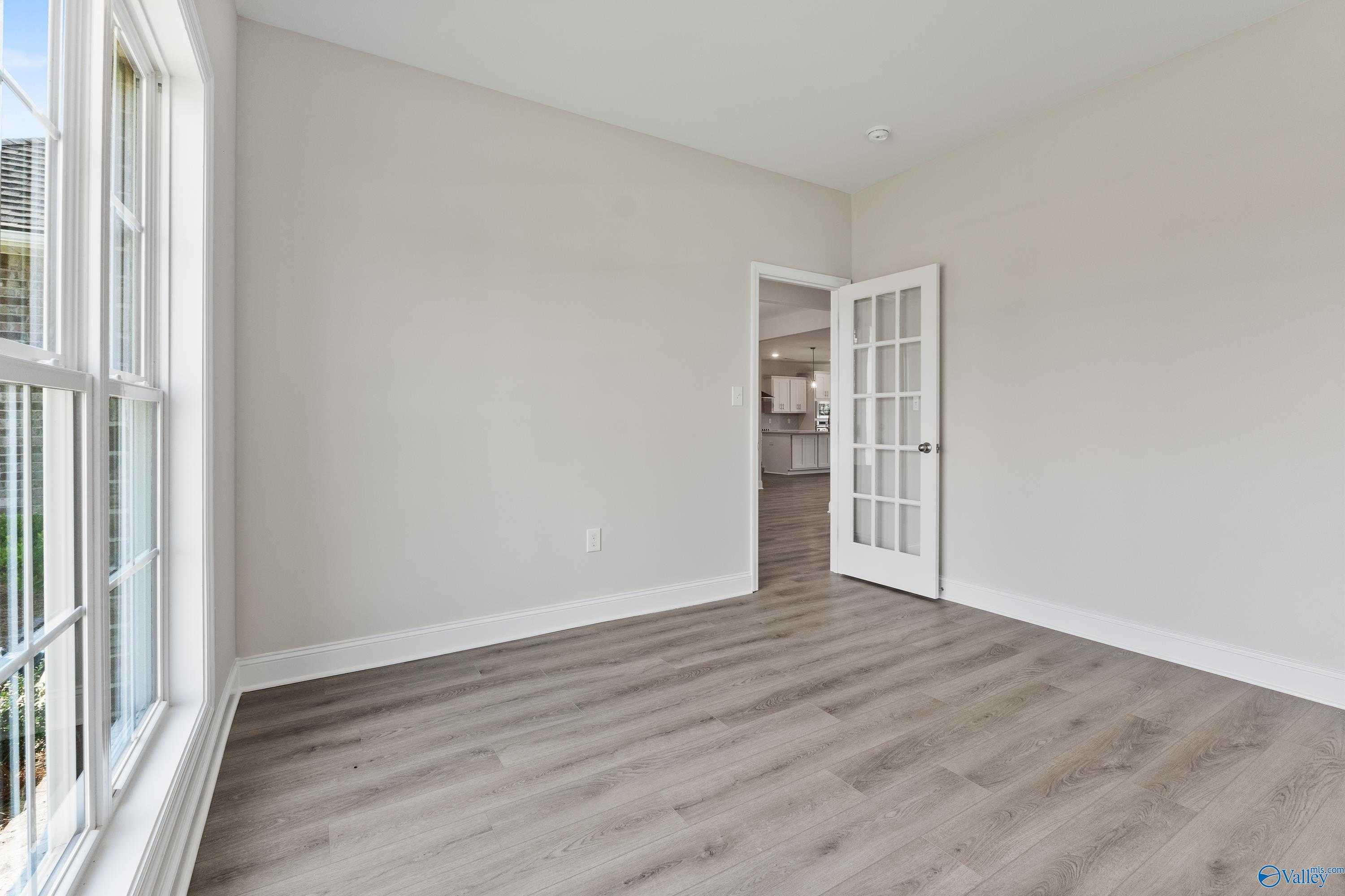Bright study with beige walls, large windows, light wood floors, and glass French door to kitchen in Davidson Homes The Finleigh, Toney, Alabama