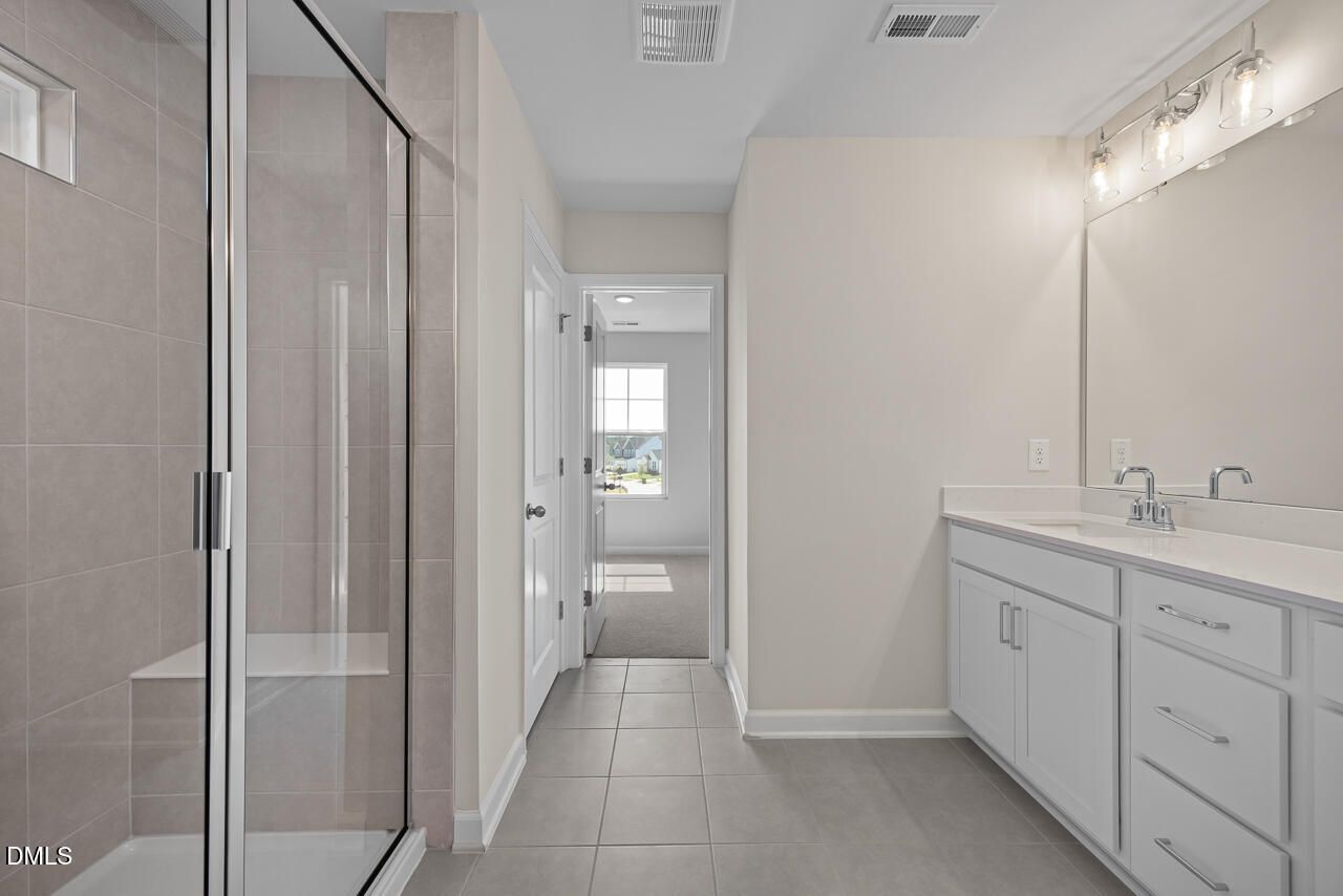 Modern primary bathroom with glass walk-in shower, dual vanity, and tile flooring in Davidson Homes The Willow C, Zebulon, NC