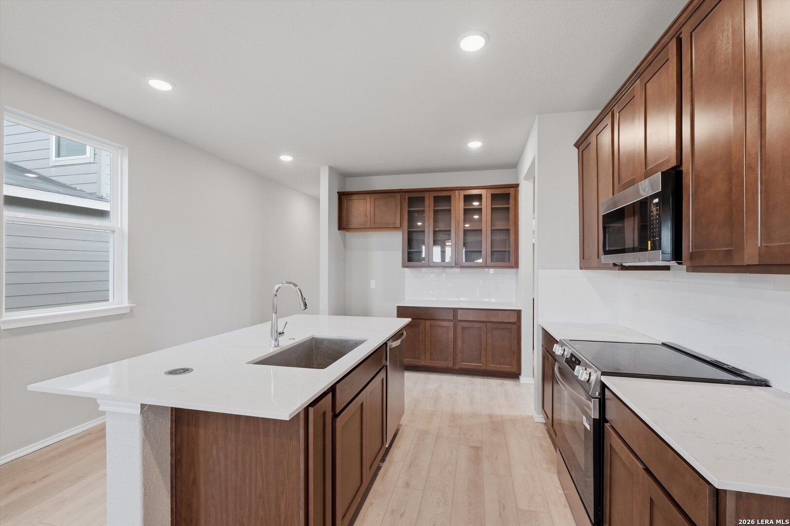 Contemporary kitchen with white quartz island, espresso shaker cabinets, stainless microwave and cooktop in The Frio B home, Agave San Antonio