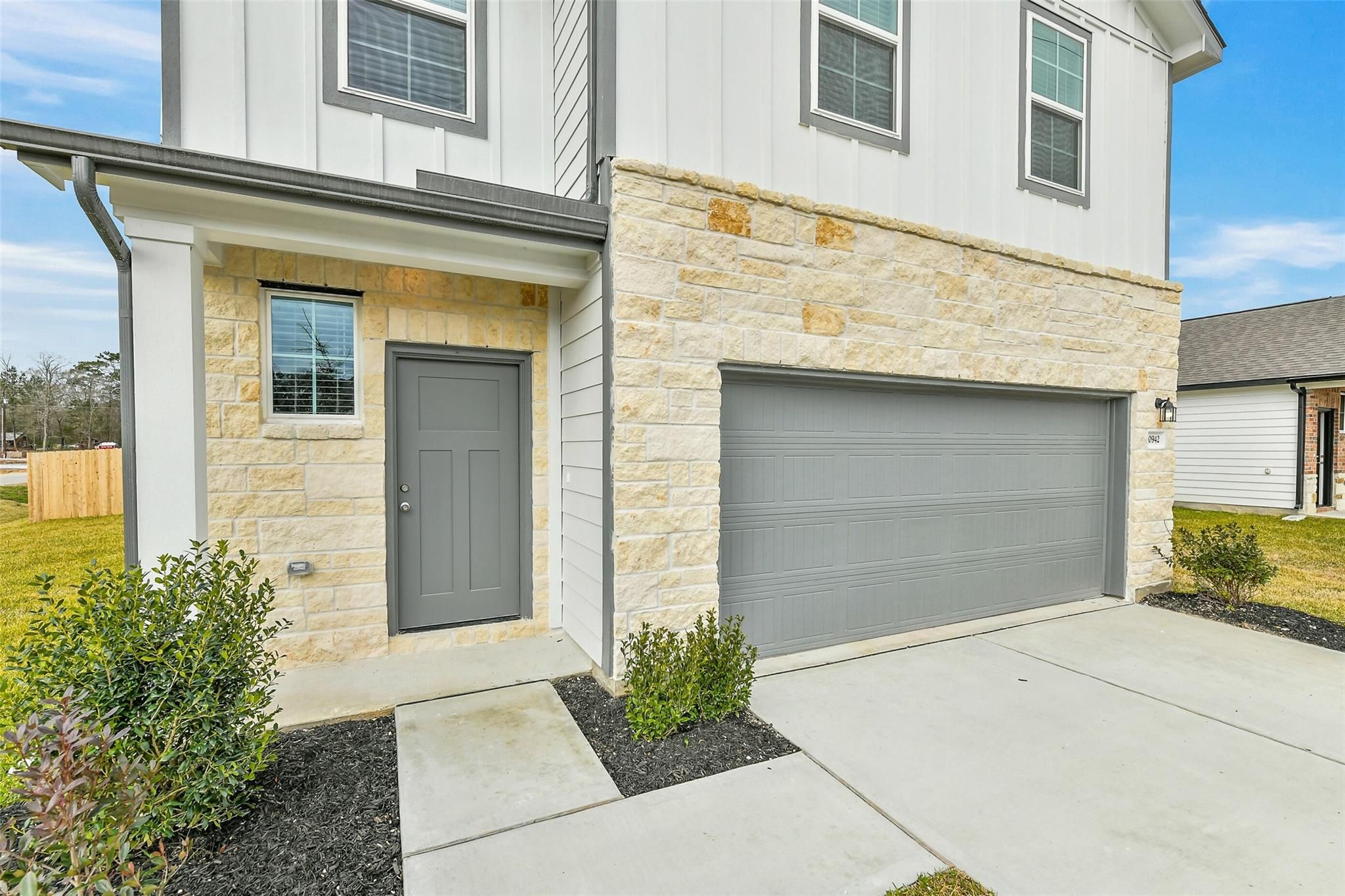 Modern two-story home exterior with stone accents, gray door, covered porch, and two-car garage in Davidson Homes The Brazos E, Liberty Estates, Cleveland, Texas