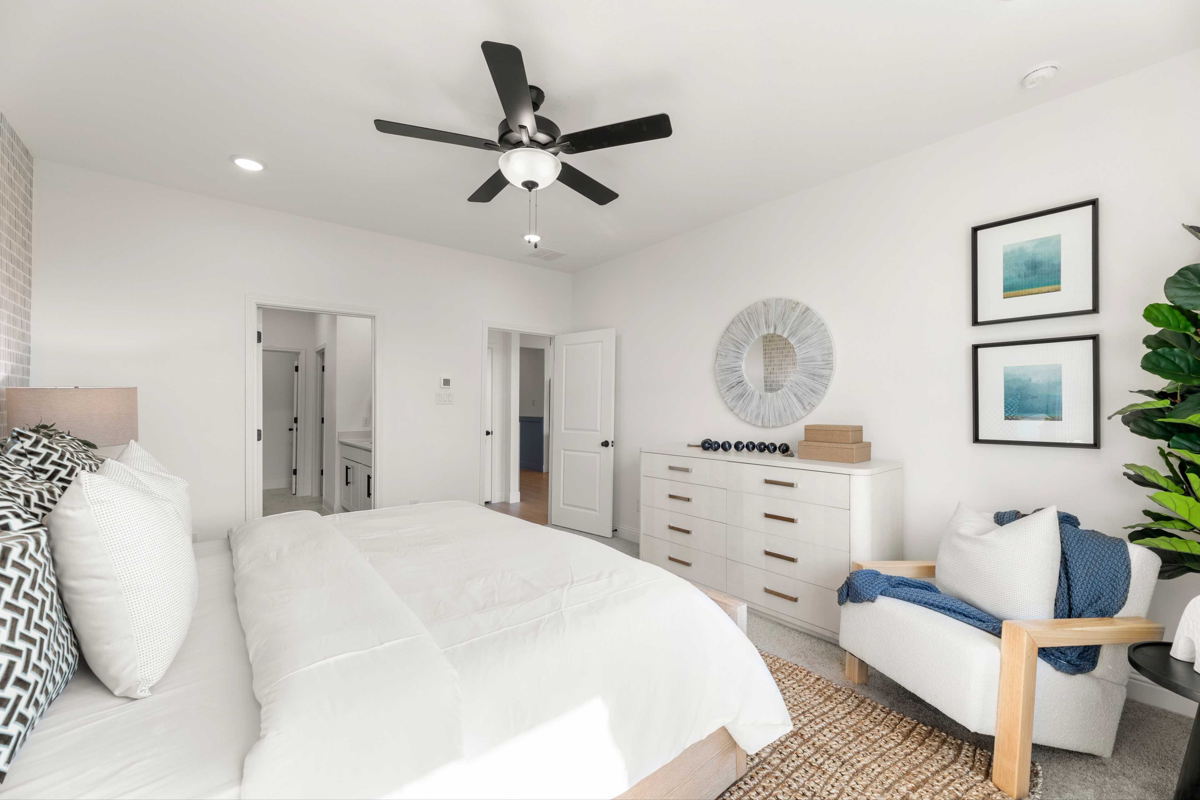 Spacious master bedroom in The Laurel I featuring king bed, ceiling fan, modern dresser, armchair, and en-suite bath door