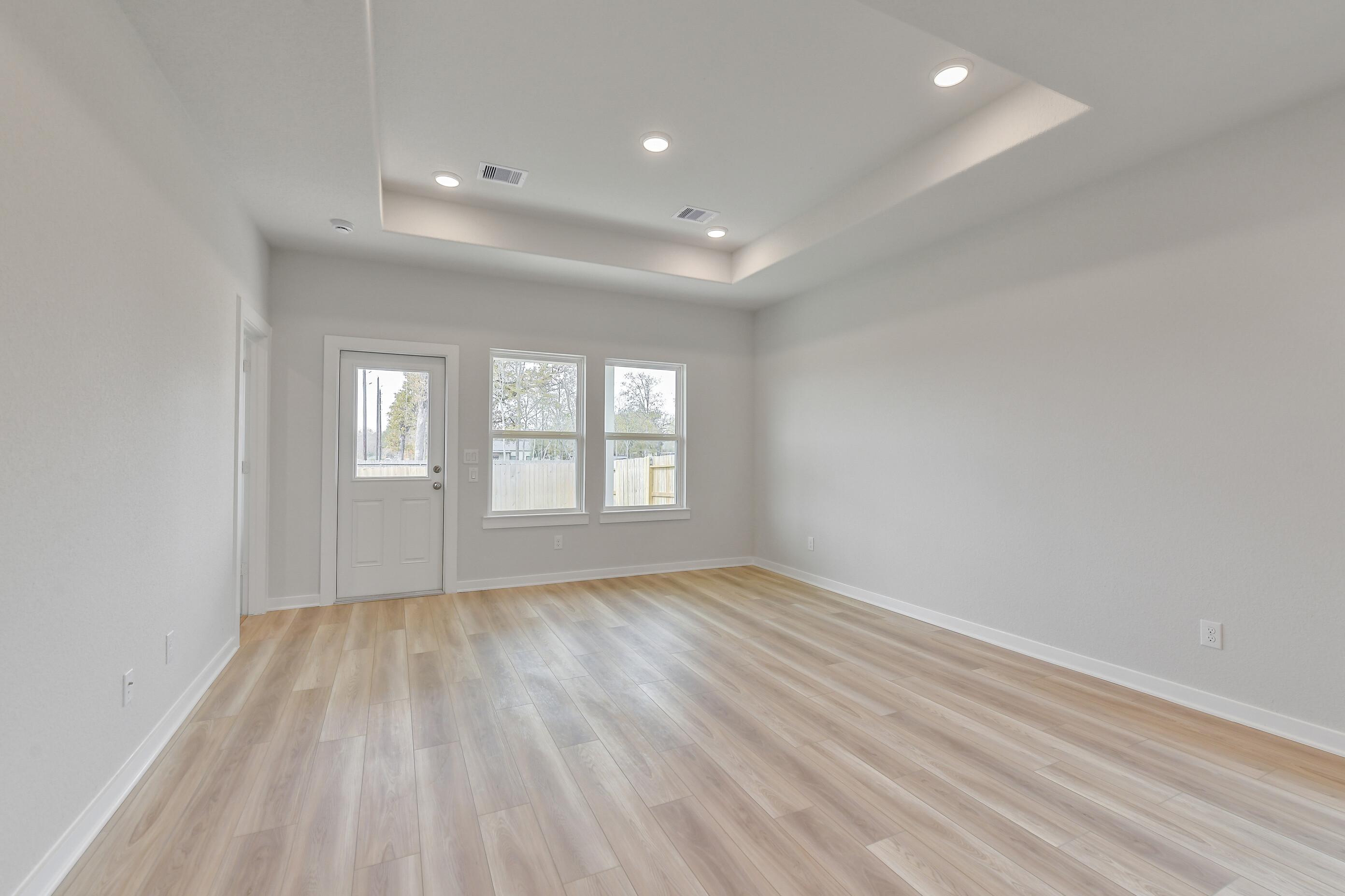 Bright living room with tray ceiling, recessed lights, light wood floors, French door, and large windows in Davidson Homes The Colorado G, Magnolia Texas