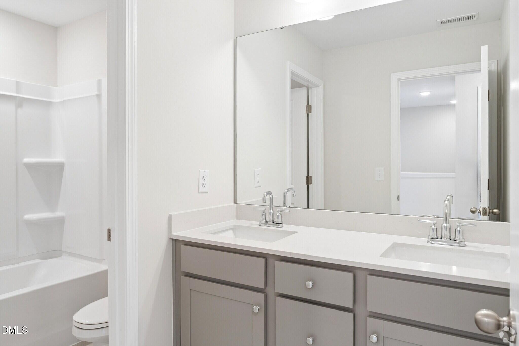 Dual-sink bathroom with gray vanity, white quartz countertop, and tub shower in Davidson Homes The Mitchell, Knightdale NC