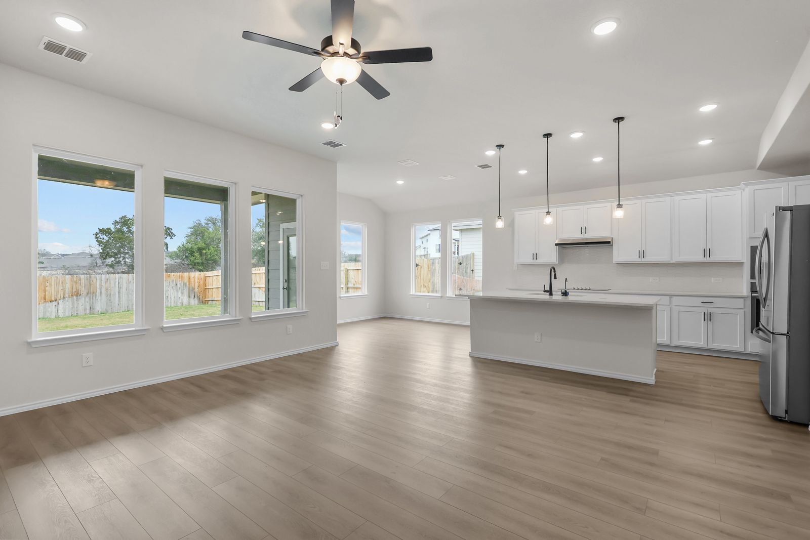 Open-concept kitchen and living area in The Sycamore B featuring white cabinetry, large island, and modern wood flooring.