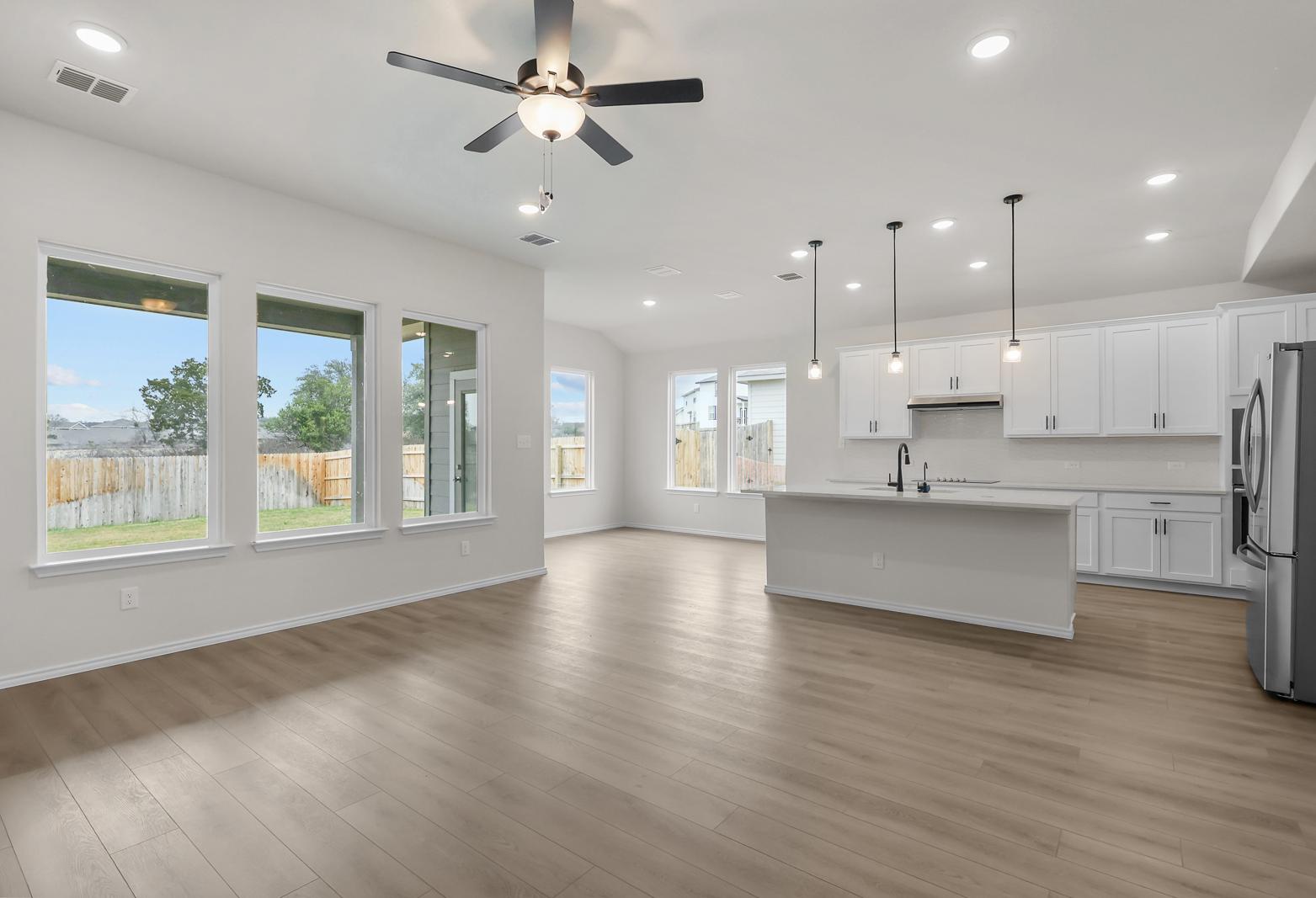 Open-concept kitchen and living area in The Sycamore B featuring white cabinetry, large island, and modern wood flooring.