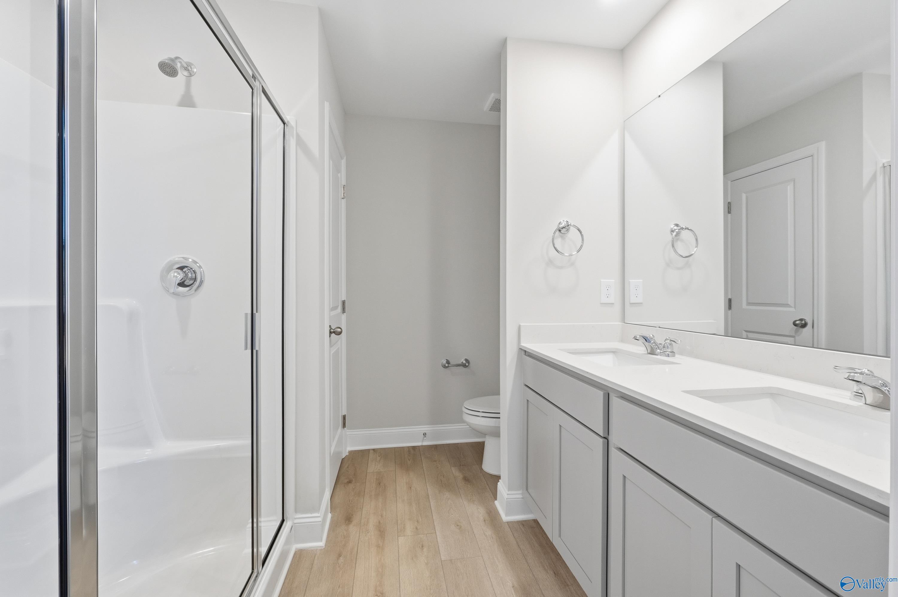 Modern master bathroom featuring dual sinks, frameless glass shower, and white shaker cabinets in Davidson Homes The Butler, New Market, Alabama
