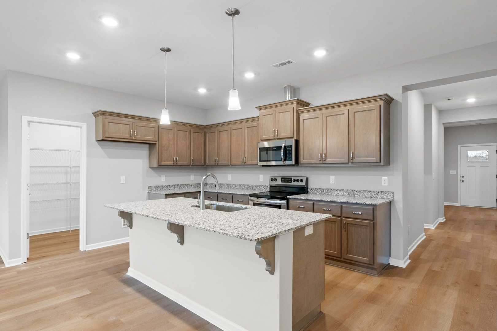Spacious kitchen in The Luna by Evermore Homes with large white island, light wood cabinets, stainless appliances, open layout
