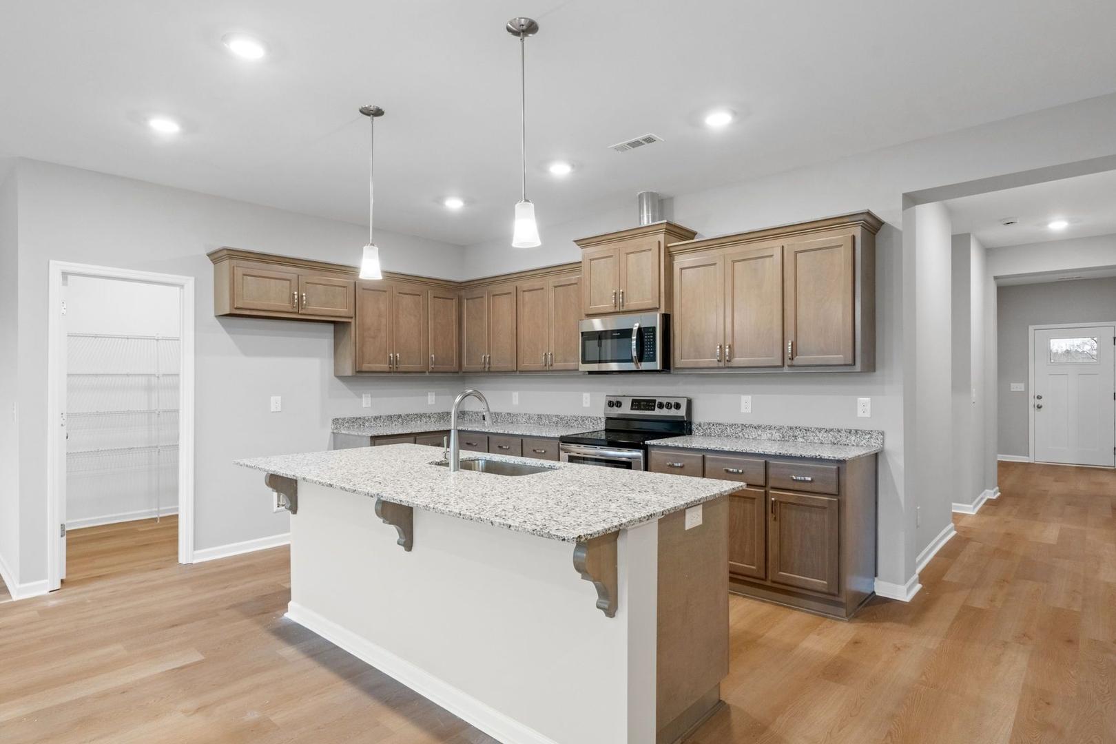 Spacious kitchen in The Luna by Evermore Homes with large white island, light wood cabinets, stainless appliances, open layout