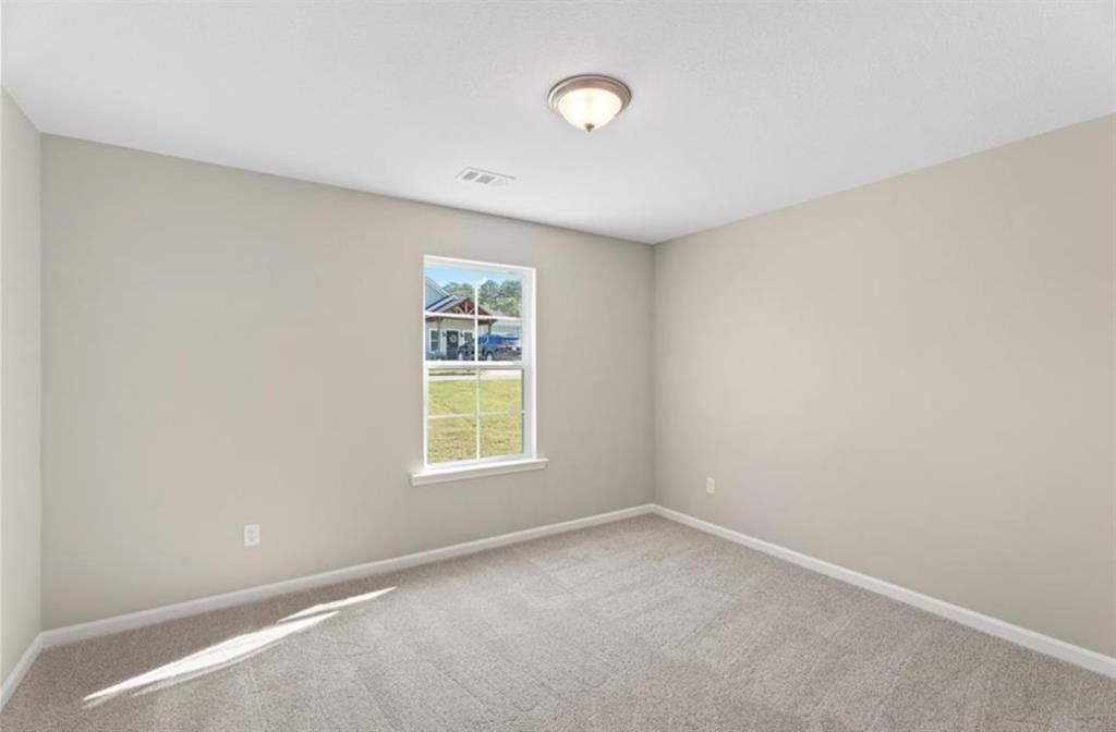 Bright secondary bedroom with beige walls, carpeted floor, and window overlooking yard in Davidson Homes The Washington, Phenix City, Alabama
