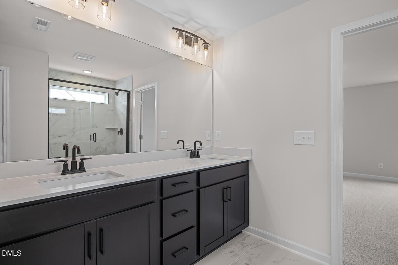 Modern bathroom with double vanity, dark cabinets, and glass shower in The Willow B floor plan at Woodland Crossing.