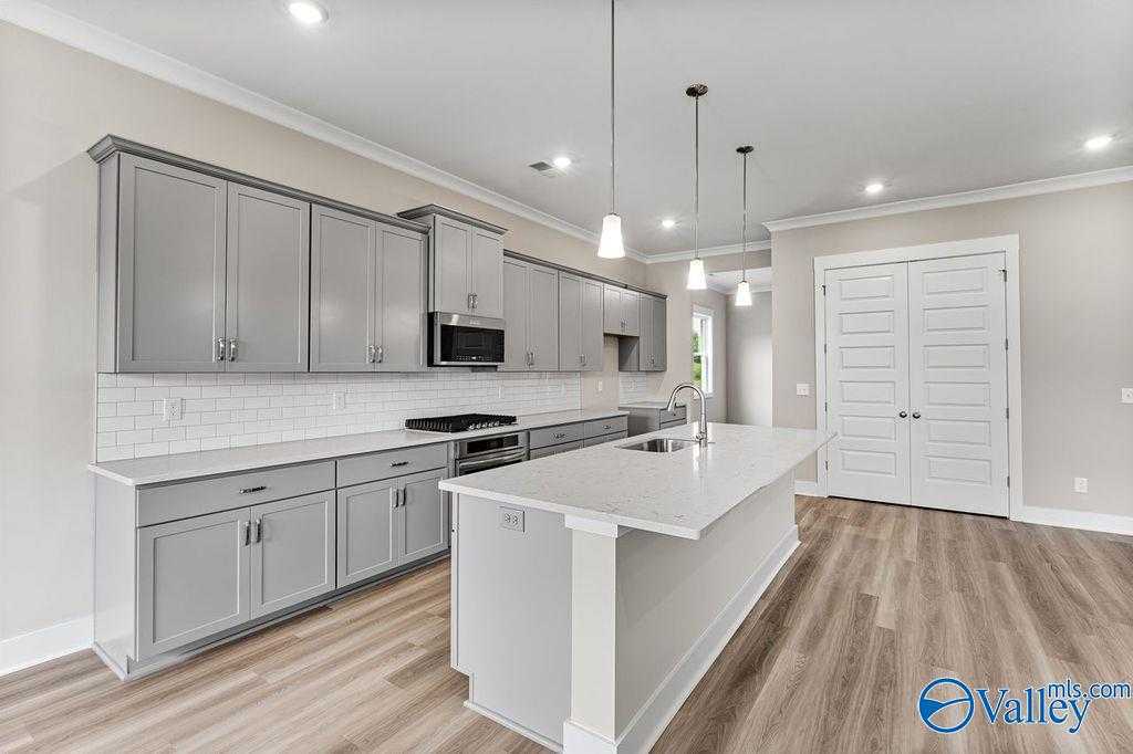 Modern kitchen with gray shaker cabinets, white quartz island, subway tile backsplash, stainless appliances in Evermore Homes The Oxford, Owens Cross Roads, AL