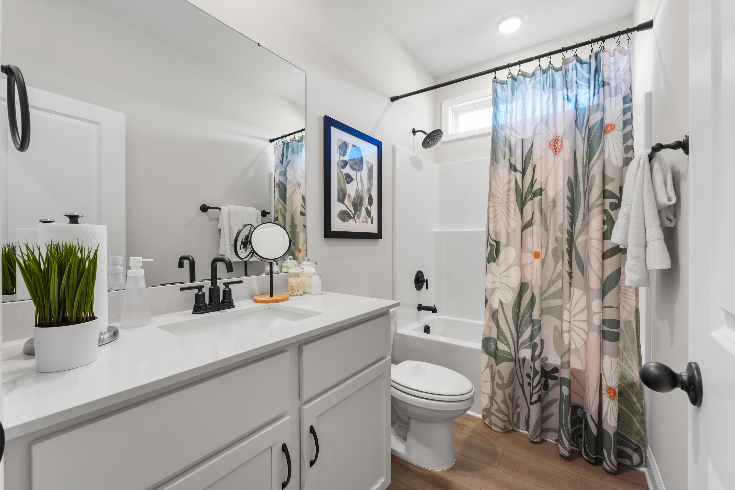Spacious modern bathroom at Mooresville Station in Tanner AL with white double vanity, floral shower curtain, tub, and hardwood floors