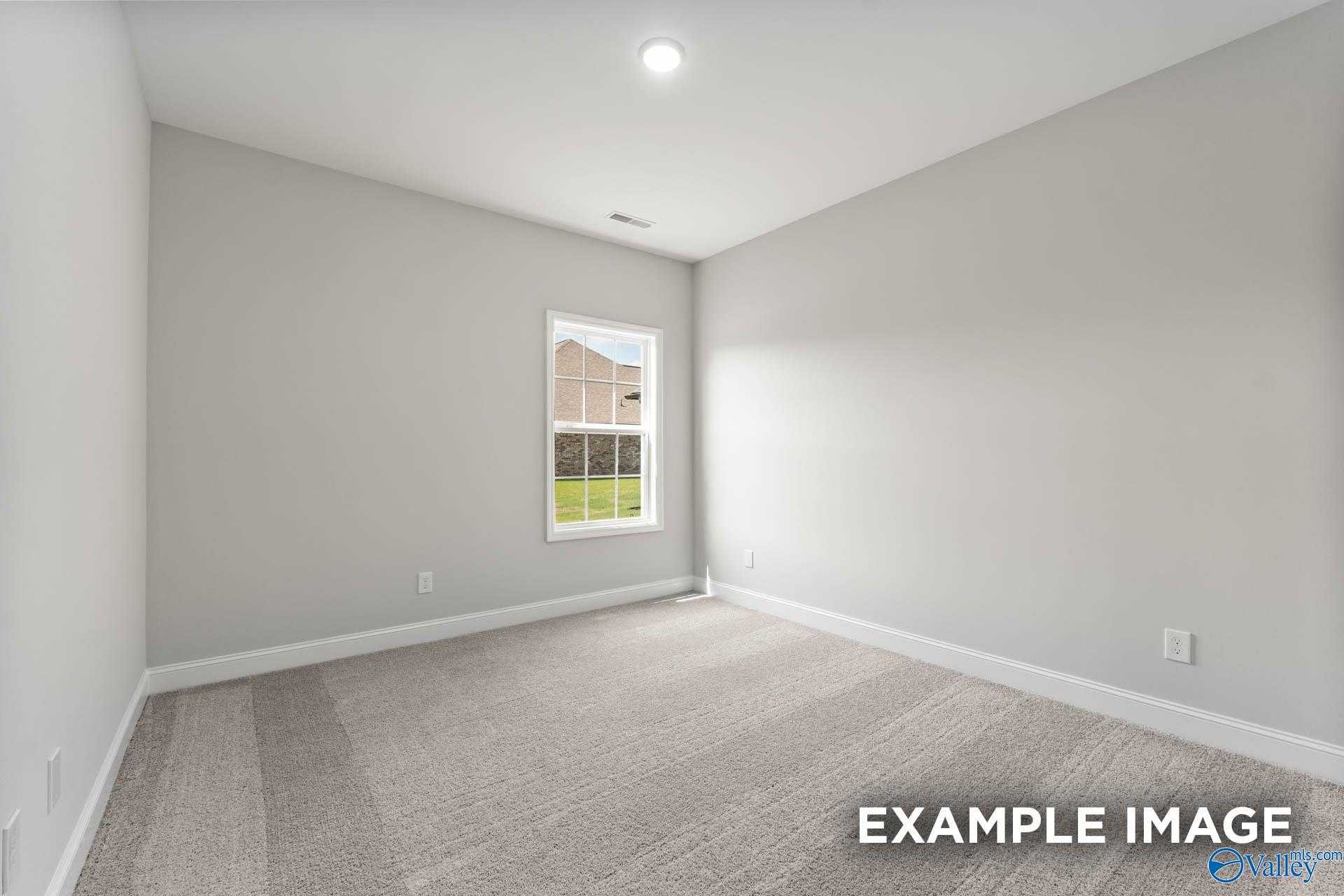 Bright empty bedroom with light gray walls, beige carpet, large window to yard in 5-bedroom Davidson Homes Madison A, Harvest AL