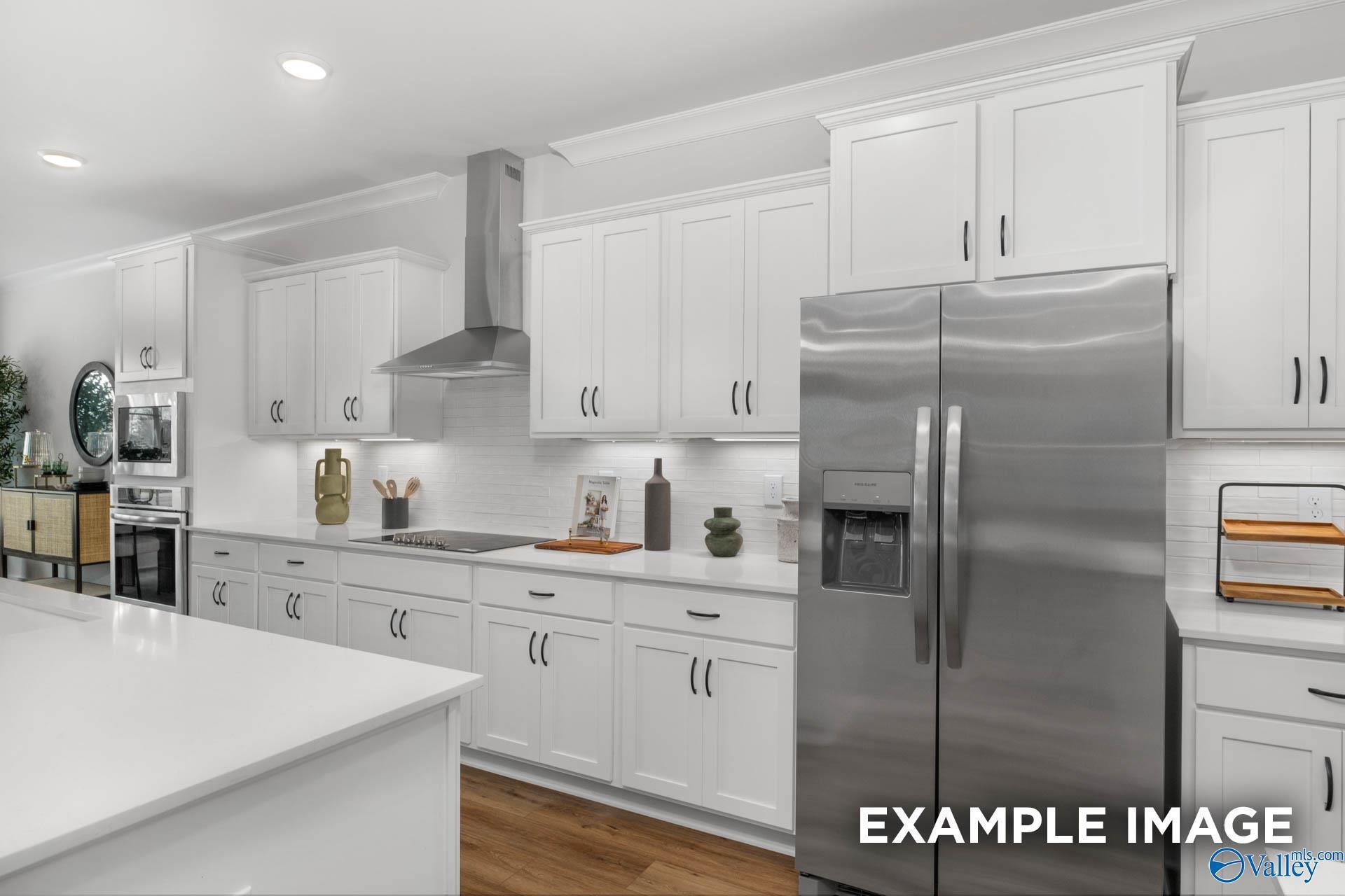 Modern white kitchen with stainless steel fridge, quartz island, and shaker cabinets in Davidson Homes The Finleigh, Decatur AL