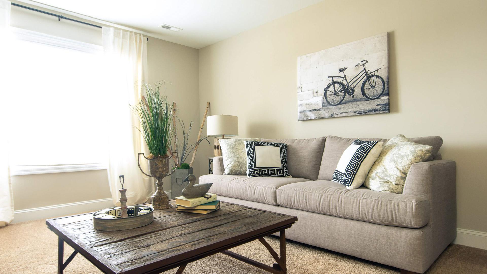 Cozy living room at Summer Pointe in Madison Alabama with beige sofa, rustic wood coffee table, bicycle wall art, and natural light