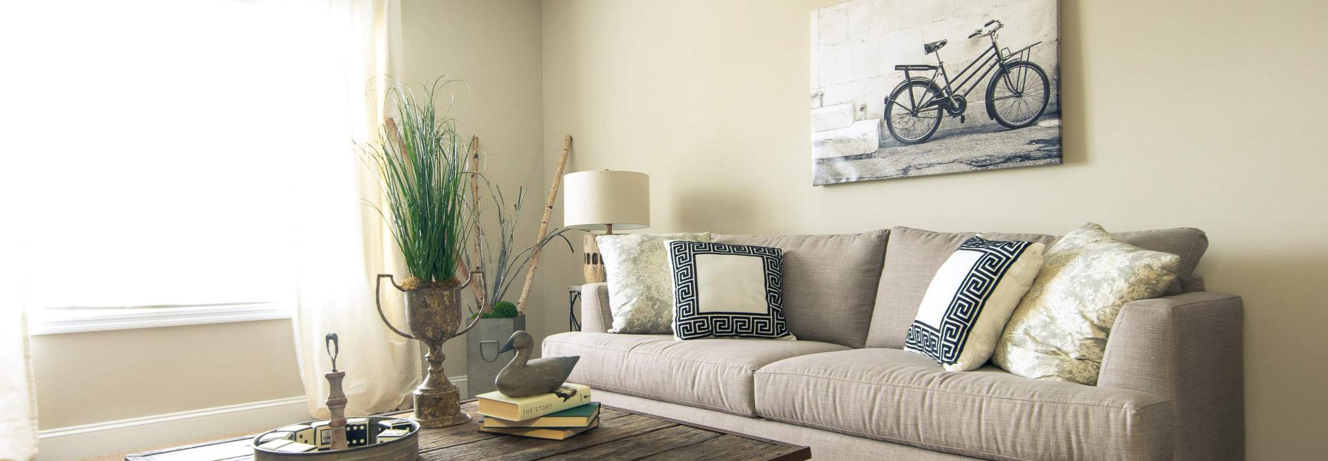 Cozy living room at Summer Pointe in Madison Alabama with beige sofa, rustic wood coffee table, bicycle wall art, and natural light