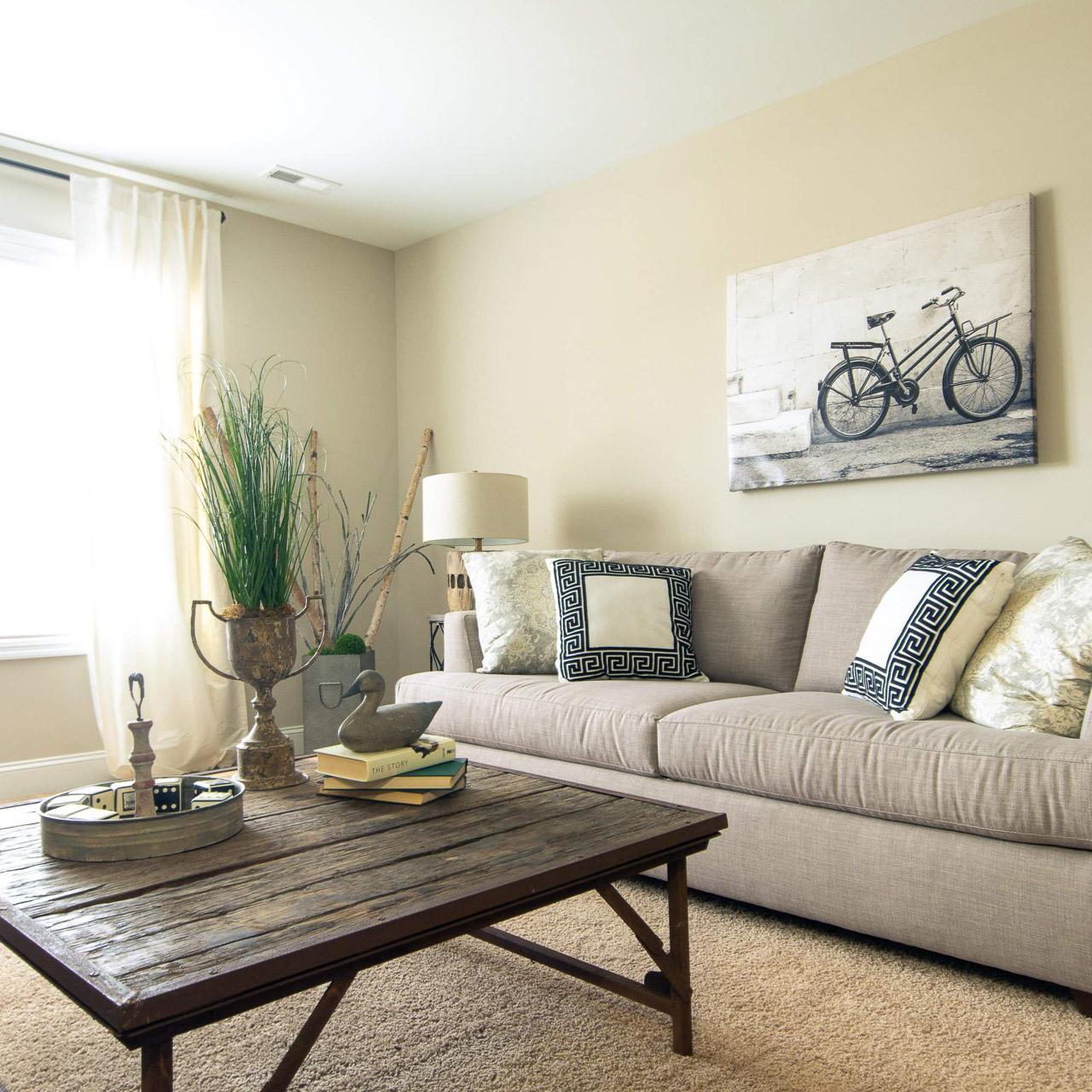 Cozy living room at Summer Pointe in Madison Alabama with beige sofa, rustic wood coffee table, bicycle wall art, and natural light