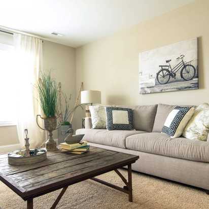 Cozy living room at Summer Pointe in Madison Alabama with beige sofa, rustic wood coffee table, bicycle wall art, and natural light